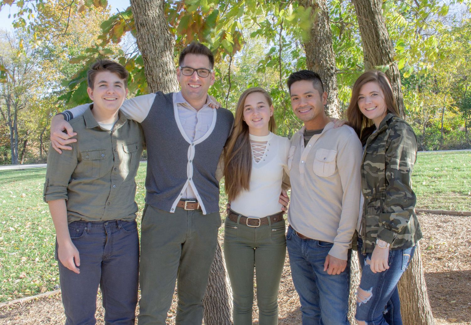 Group portrait in casual attire standing together under autumn trees.