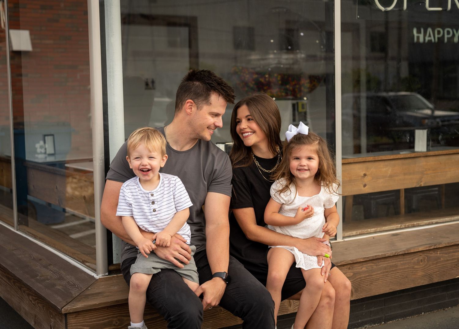 A relaxed family moment captured on wooden steps outside a storefront.