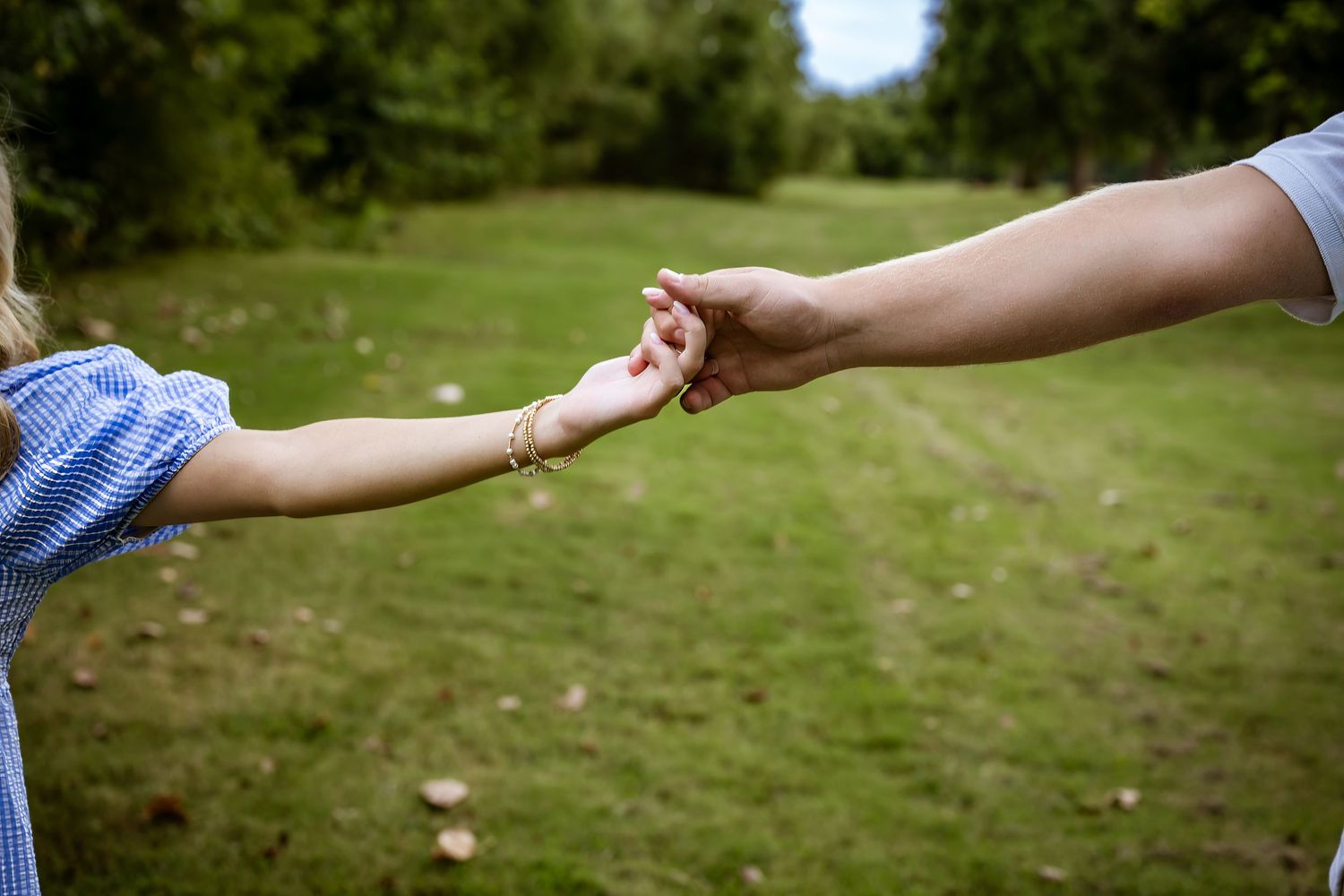 Close up of two hands reaching to hold each other in a grassy outdoor setting.