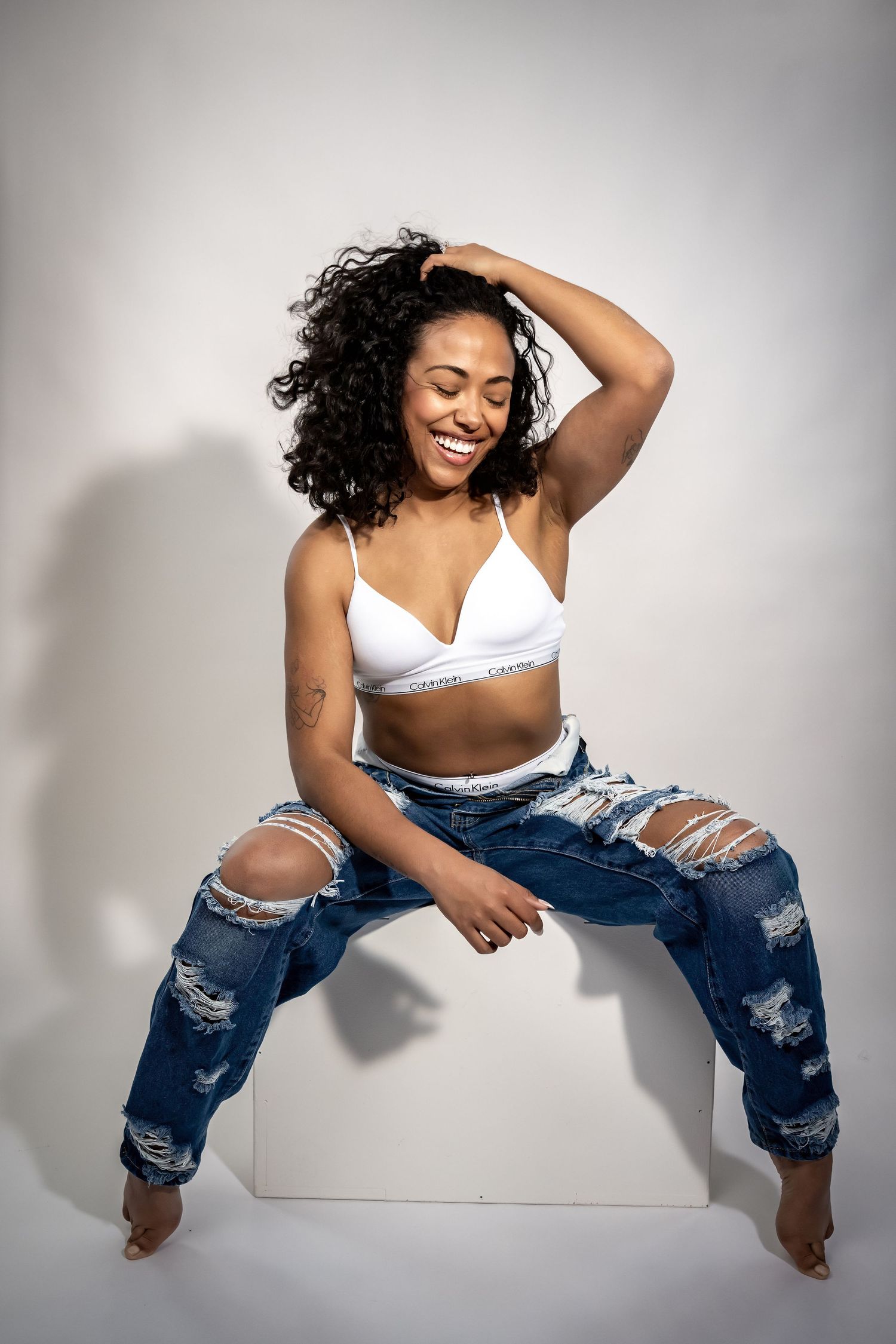 Model in distressed denim and white top strikes playful poses on white backdrop.