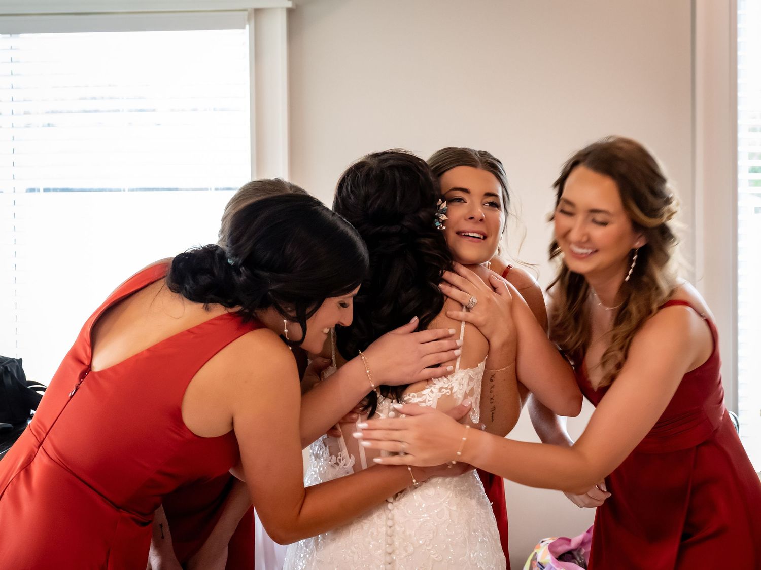 Emotional group hug between people wearing red dresses in a bright room.