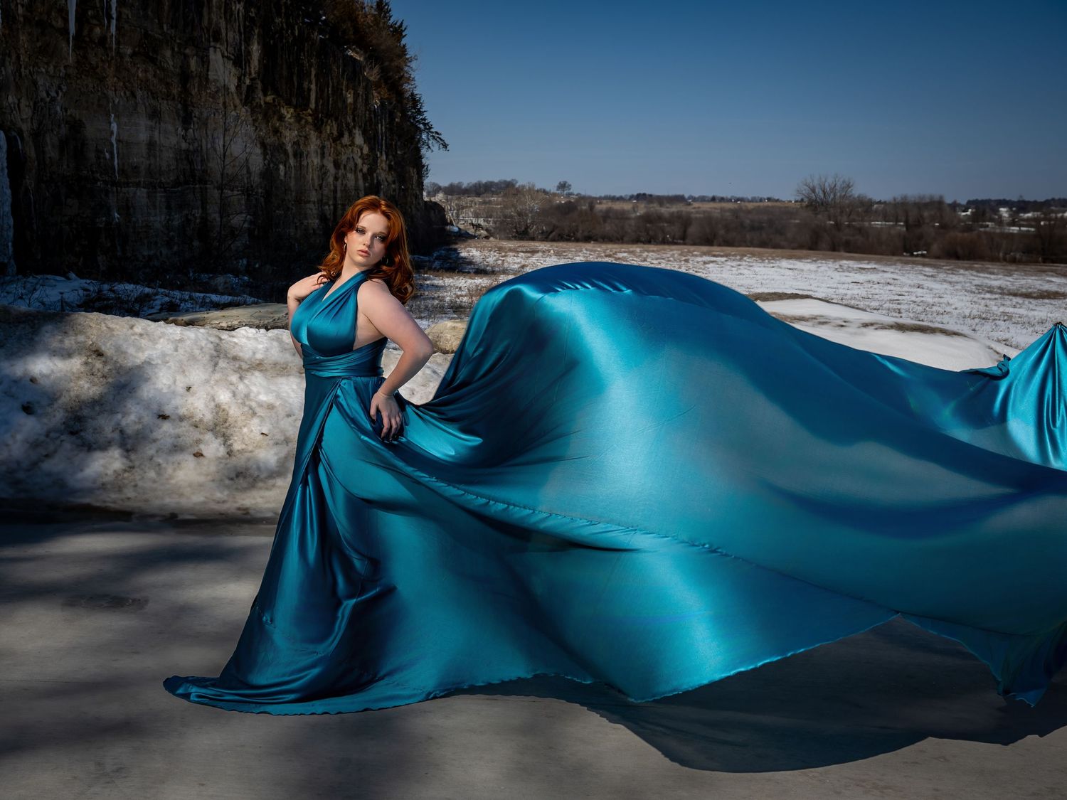 Flowing turquoise fabric creates graceful waves against a snowy winter landscape with bright blue sky.