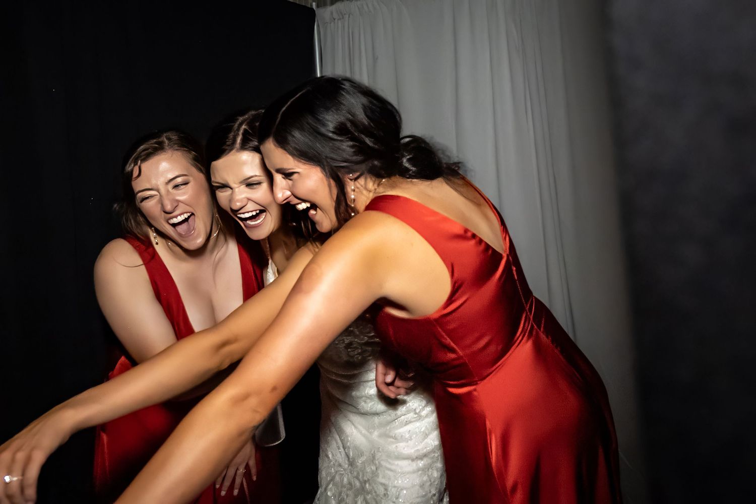 Wedding party in red bridesmaid dresses and white gown share joyful moment together.