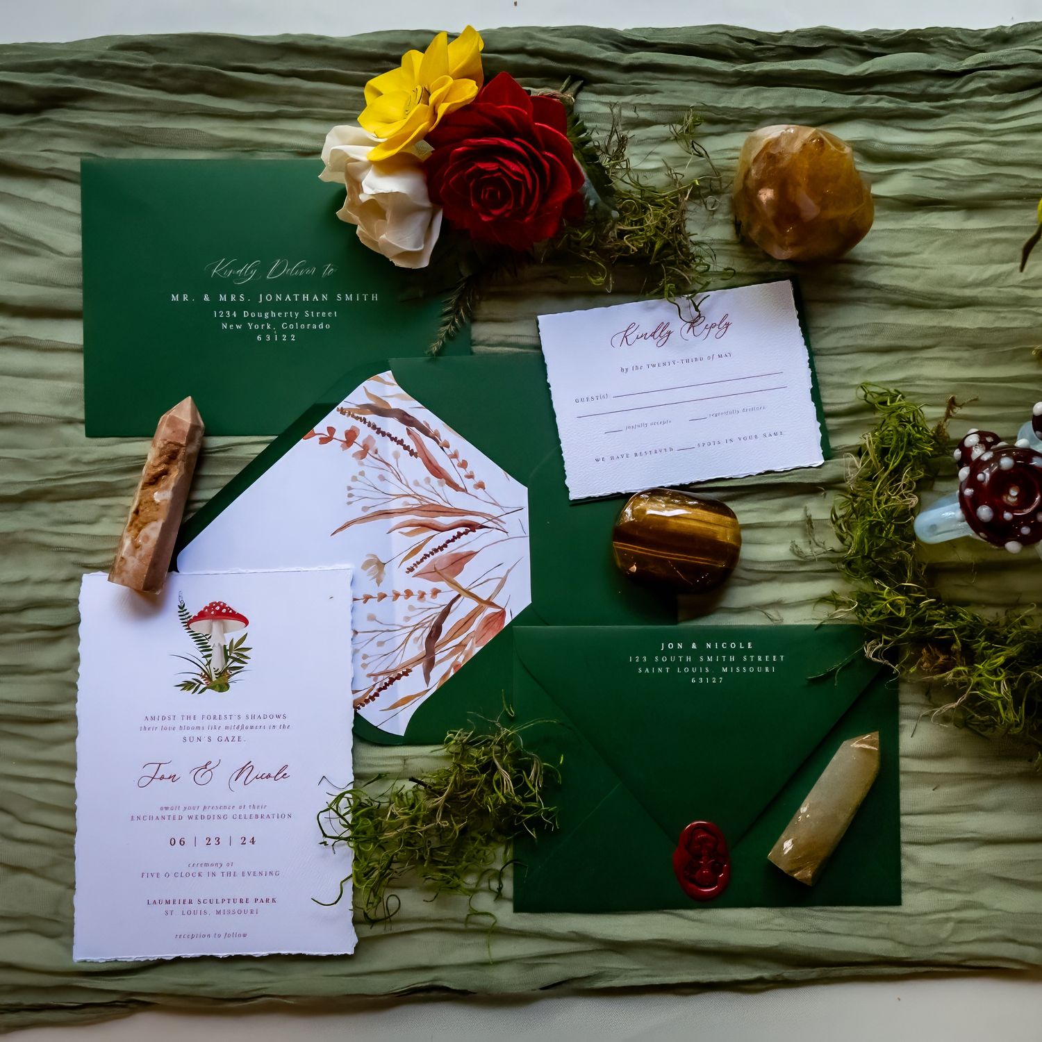 Wedding invitations with floral designs laid out on dark green fabric with scattered flowers.