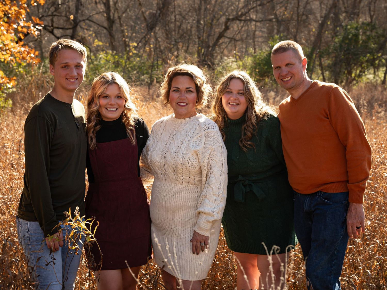 Group of five people in autumn clothing posing together in a golden fall setting.