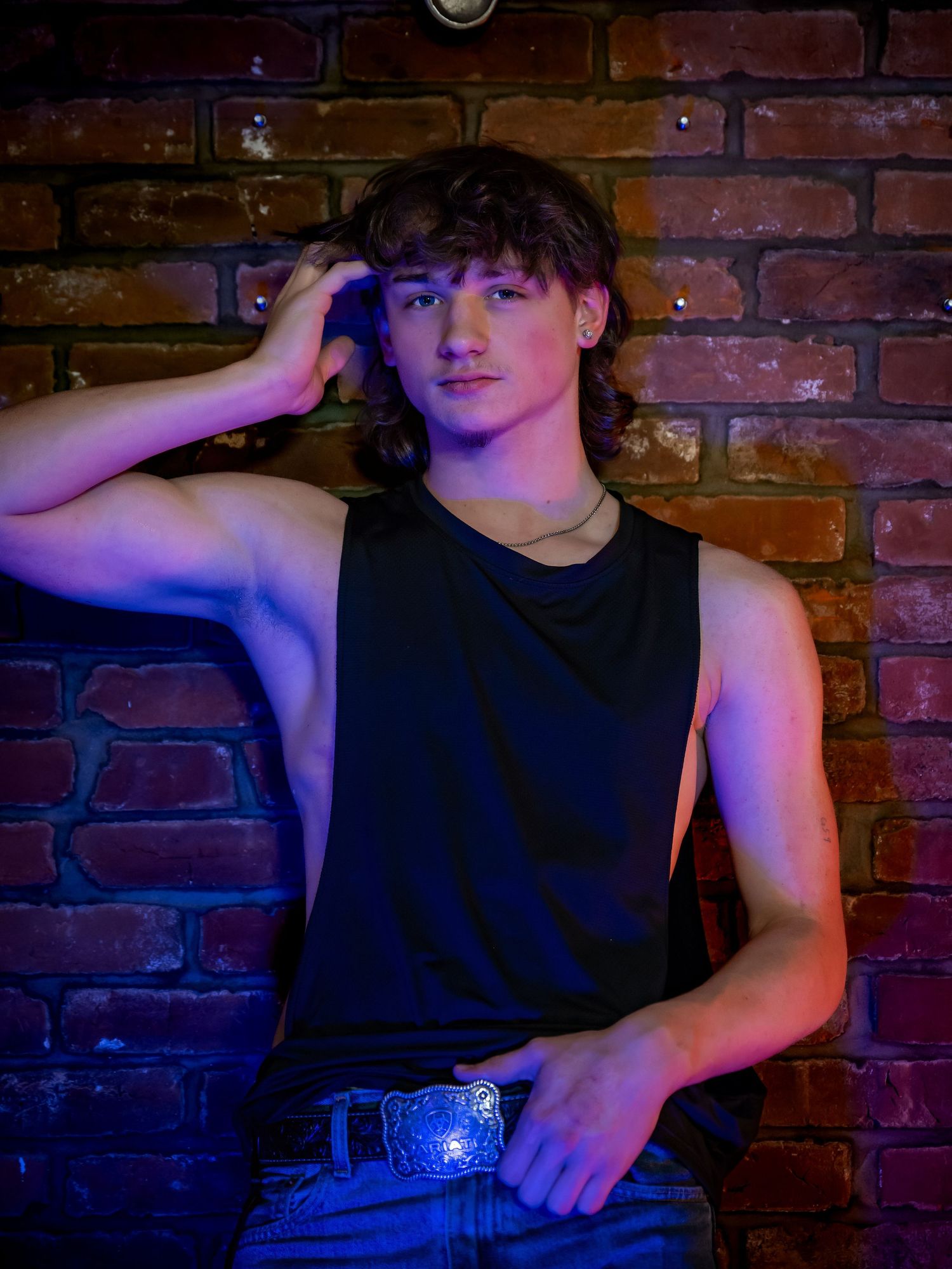 Dramatic portrait with neon lighting against brick wall background.