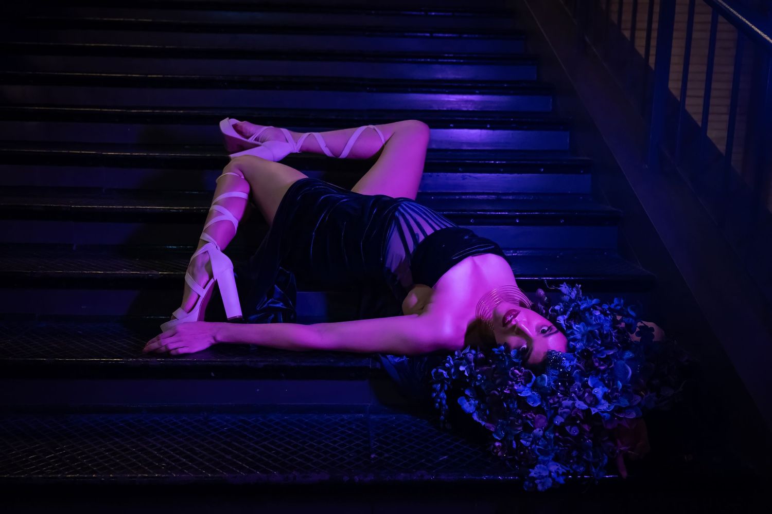 Artistic low-light photo on stairs with purple lighting and floral elements.