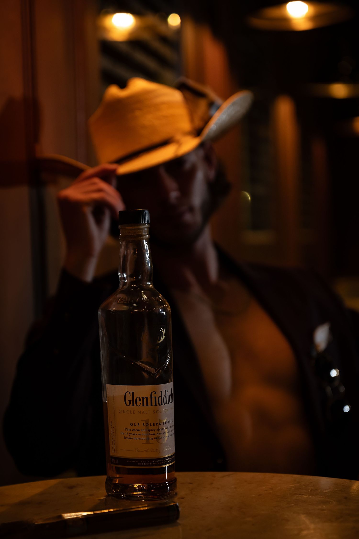 Bottle of Glenfiddich whiskey on a dark wooden surface under warm lighting.