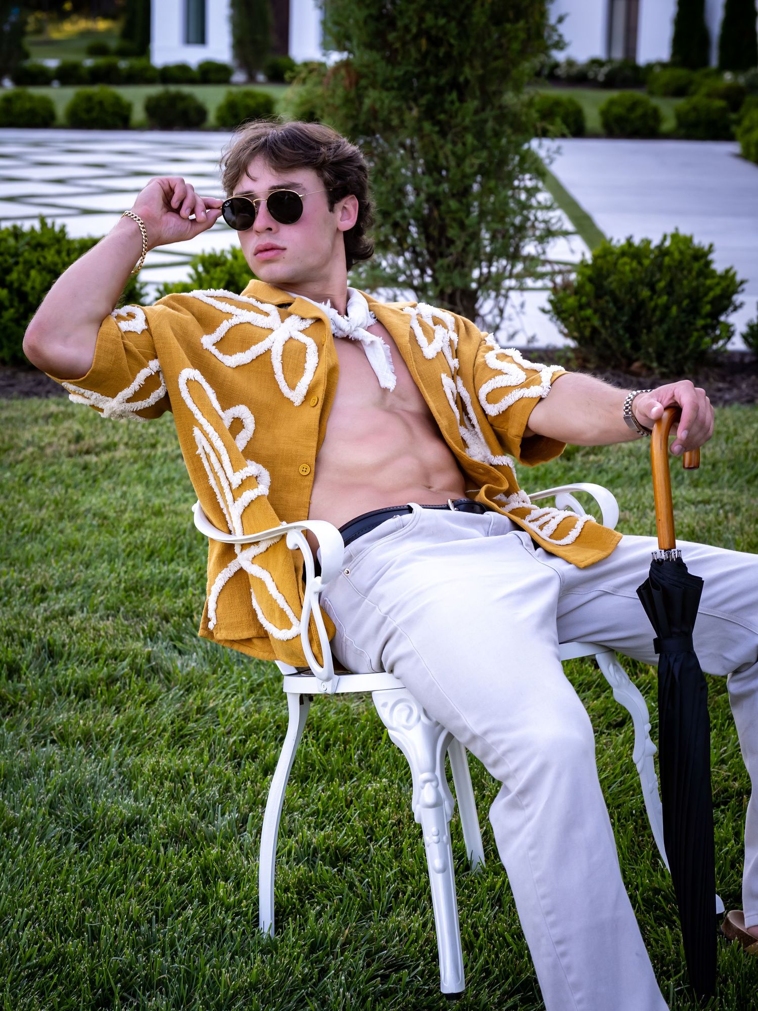 Person lounging in chair wearing yellow patterned shirt and white pants outdoors.