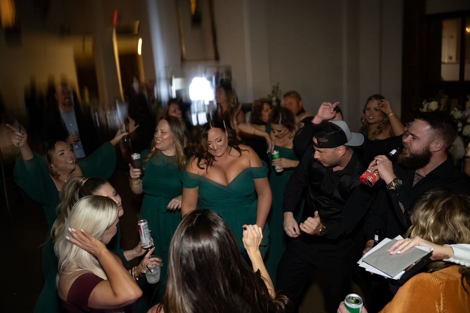 Wedding reception crowd dances and celebrates in dark venue with ambient lighting.