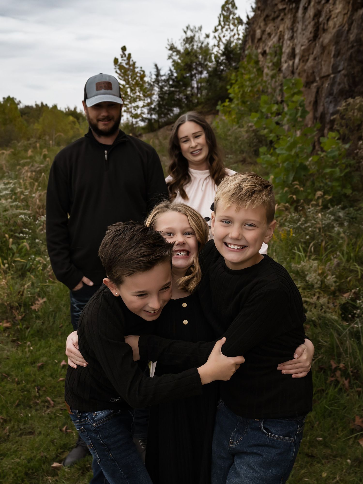 A family shares joyful moments together in an outdoor photoshoot against a natural wooded backdrop.