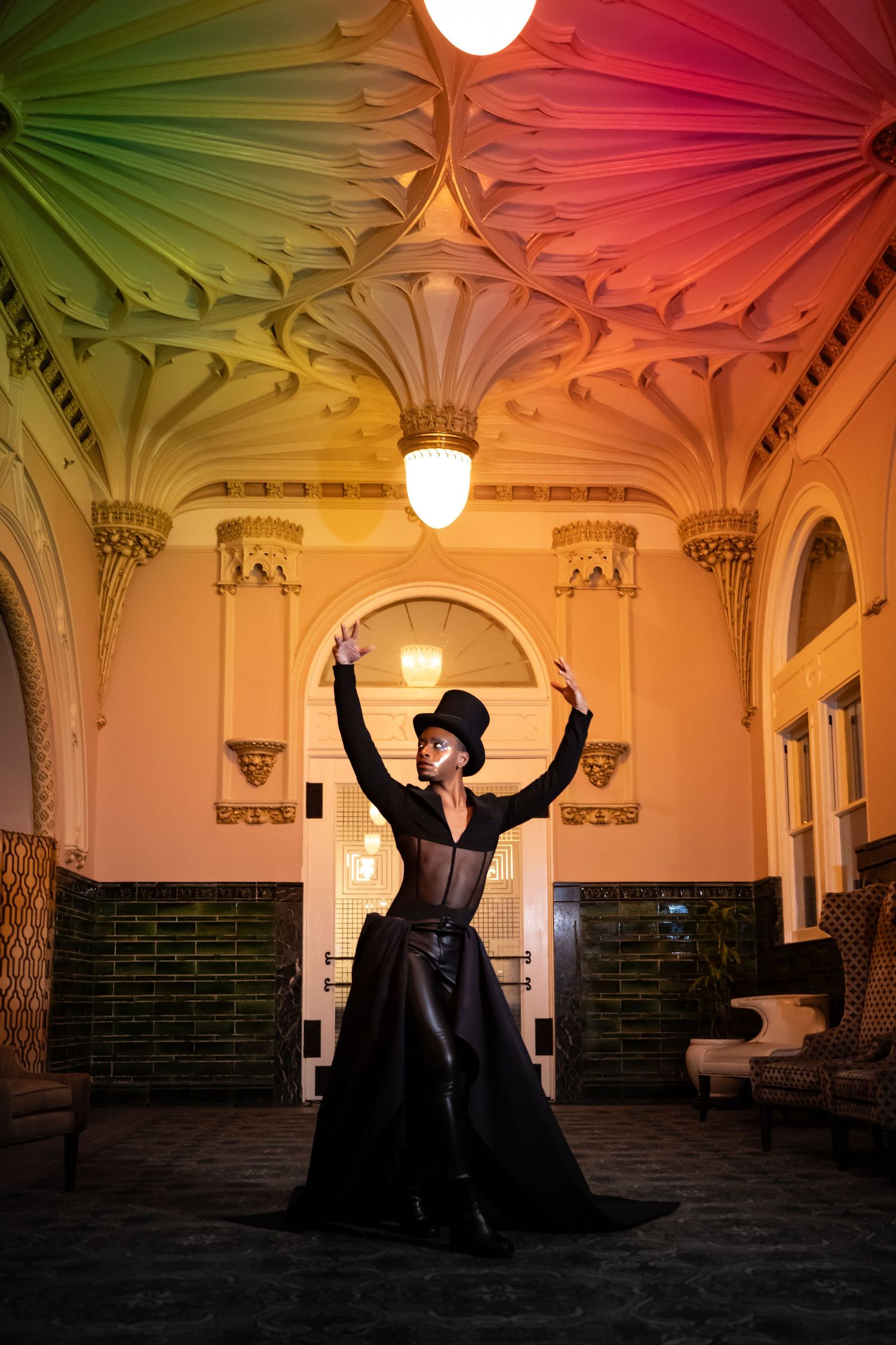 A silhouetted figure performs expressive dance movements in a historic building with ornate architectural details and warm lighting.