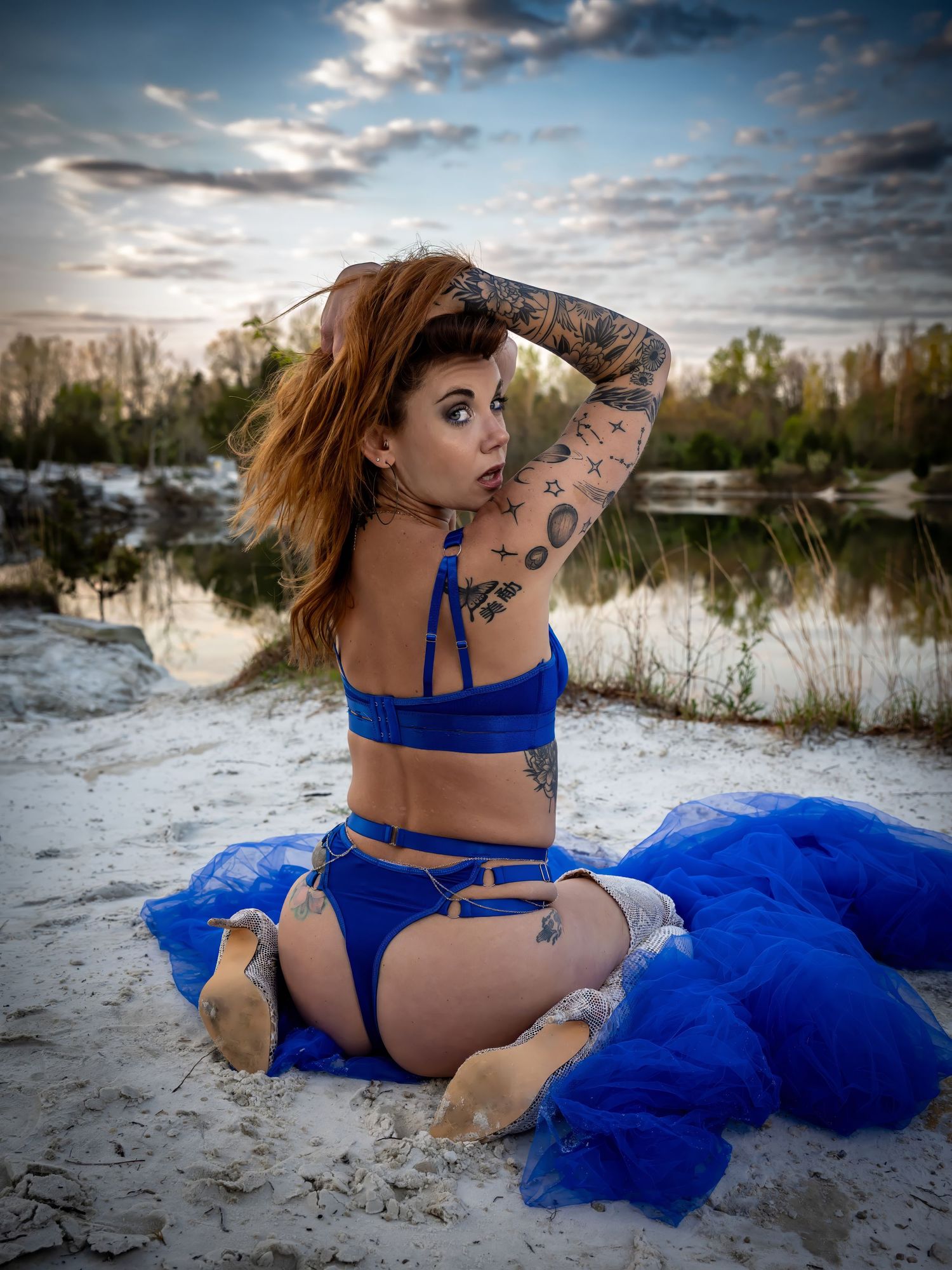 Person in royal blue outfit poses on sandy beach with dramatic sky.