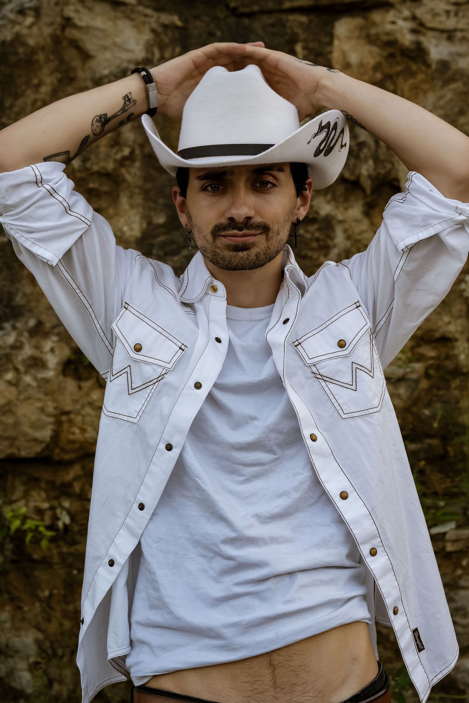 A western-style portrait featuring a white cowboy hat and denim jacket against a rocky backdrop.