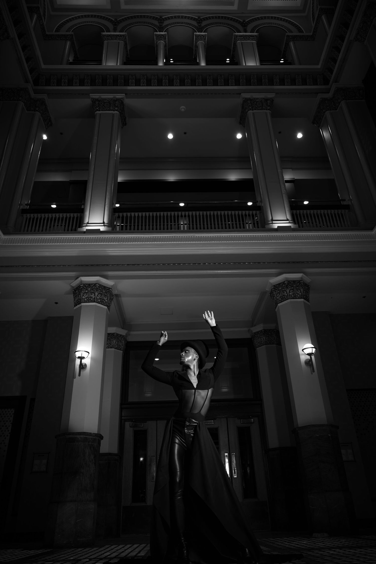 Black and white photo of performer in dramatic pose beneath grand architectural columns.