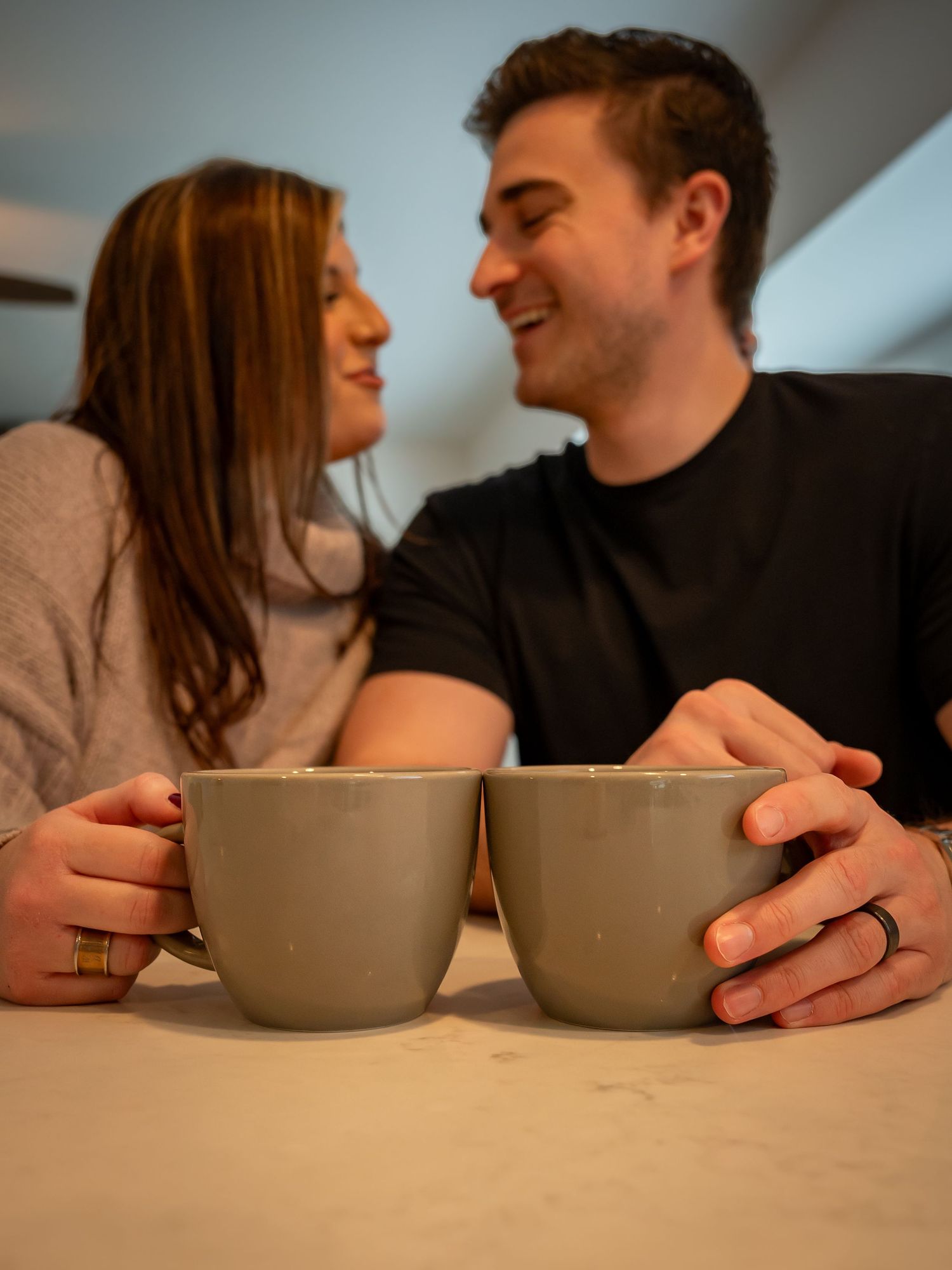 Two people share an intimate moment over coffee in gray ceramic mugs.