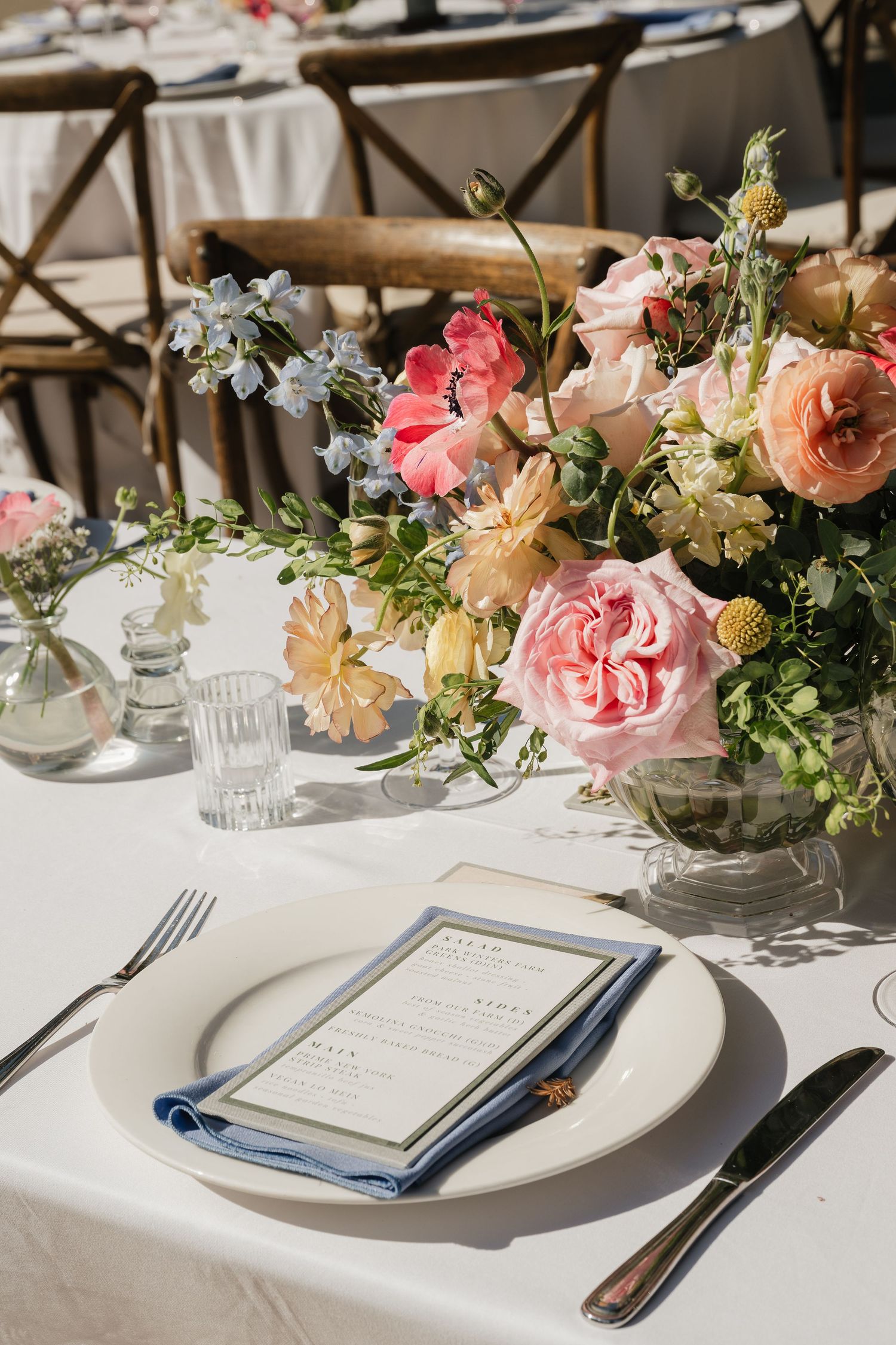 Elegant wedding table setting with pink floral centerpiece, white linens, and menu card on white china plate.