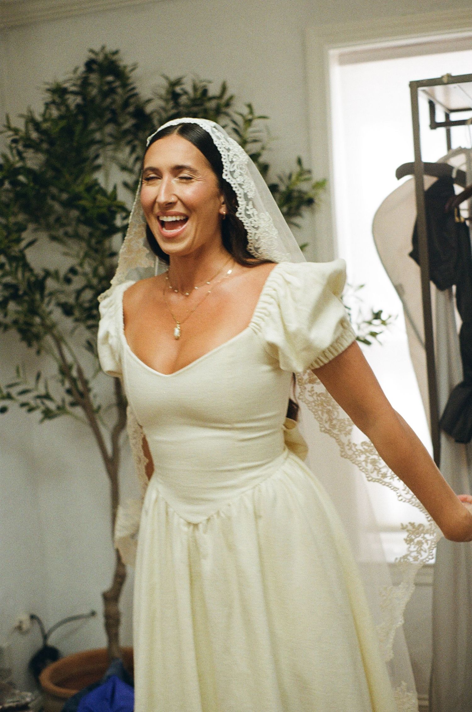 A bride in an empire waist ivory gown and lace veil smiles during her wedding day photo session.