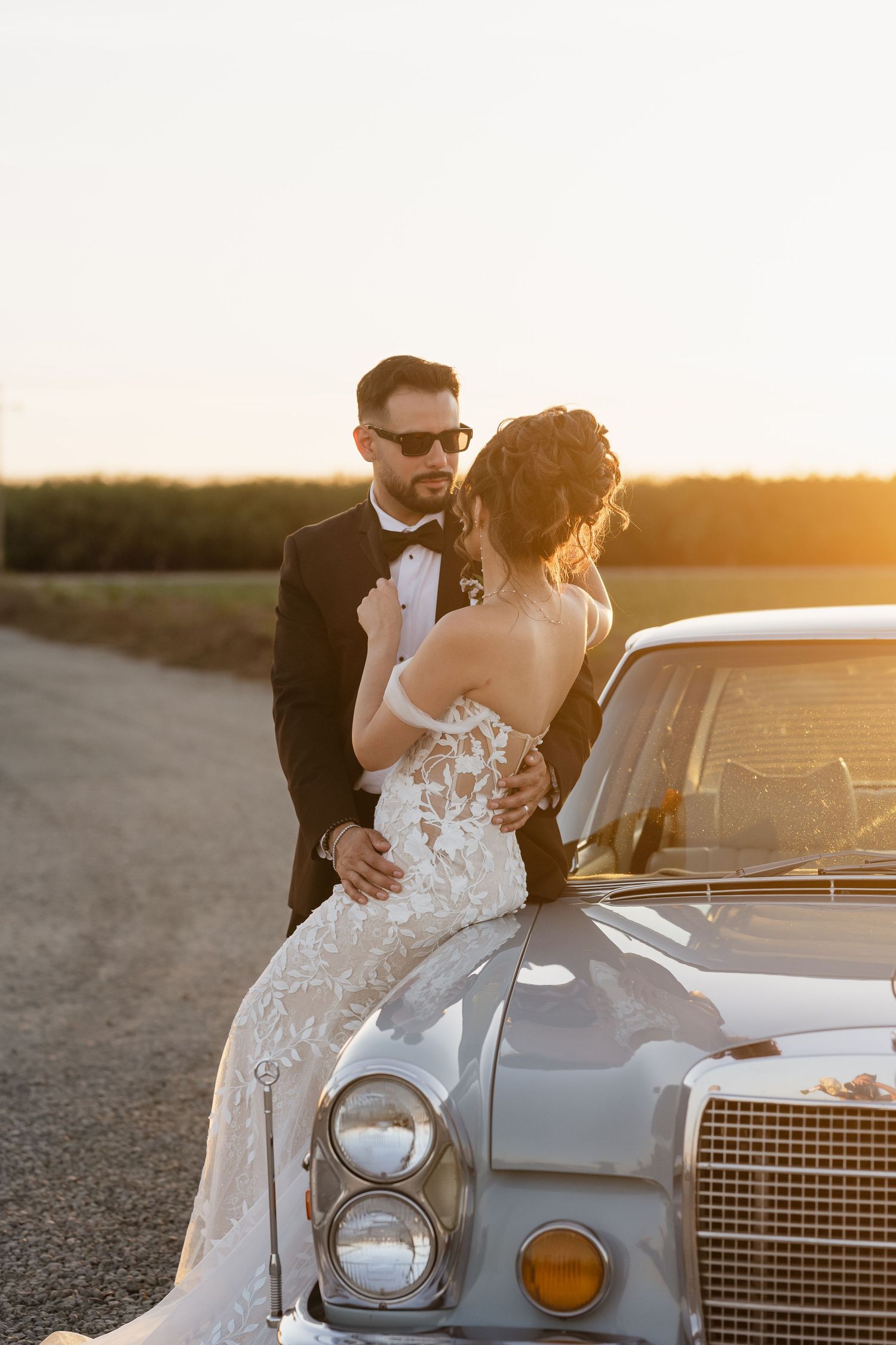 A couple poses with a classic vintage car during their wedding sunset photoshoot.