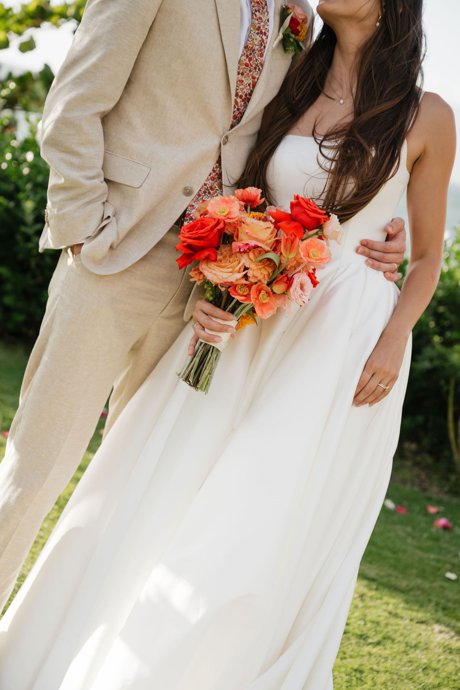Wedding party detail showing coral bouquets against white dress and tan suit.
