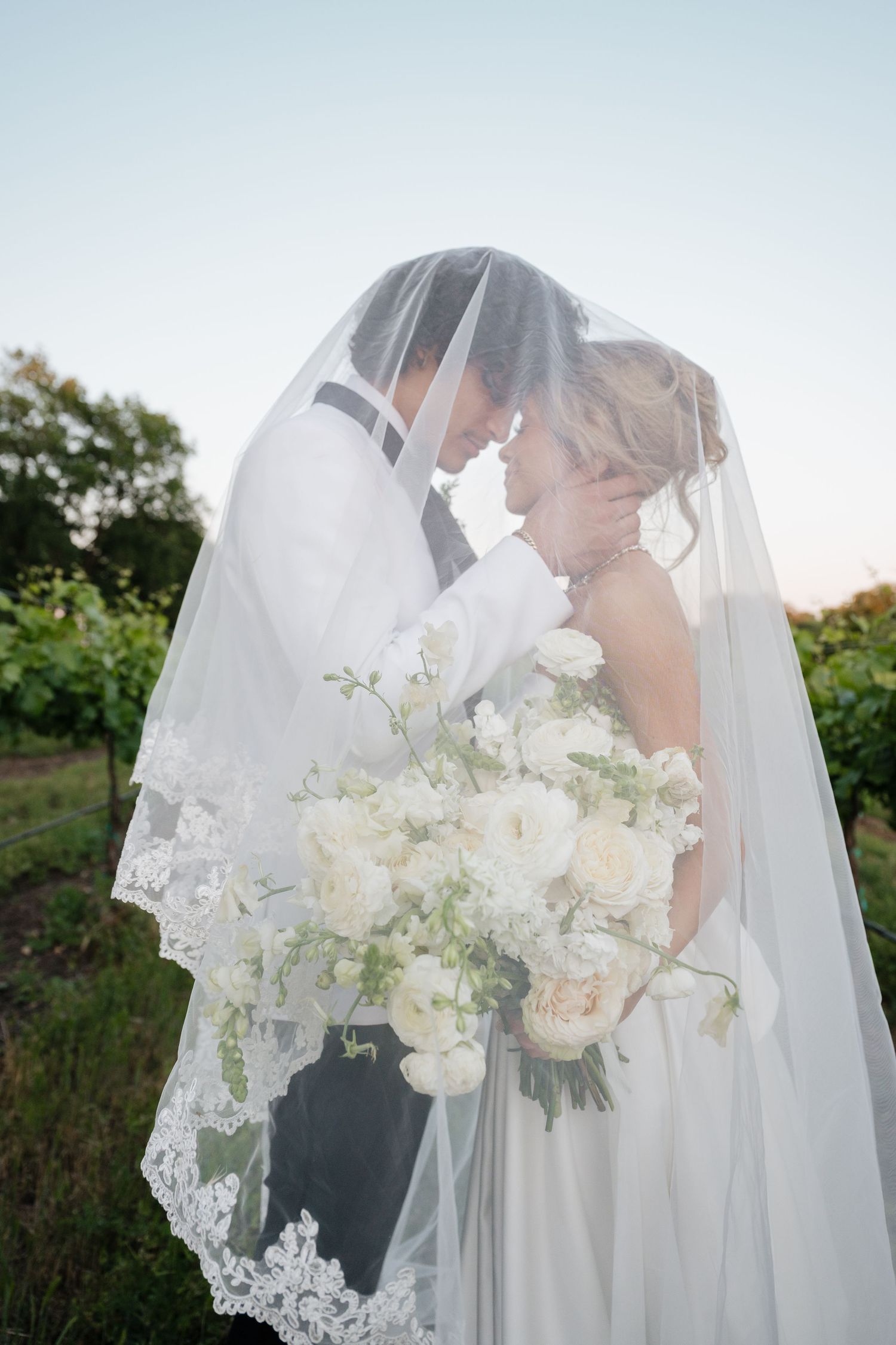 Romantic wedding portrait through delicate lace veil with white floral bouquet.