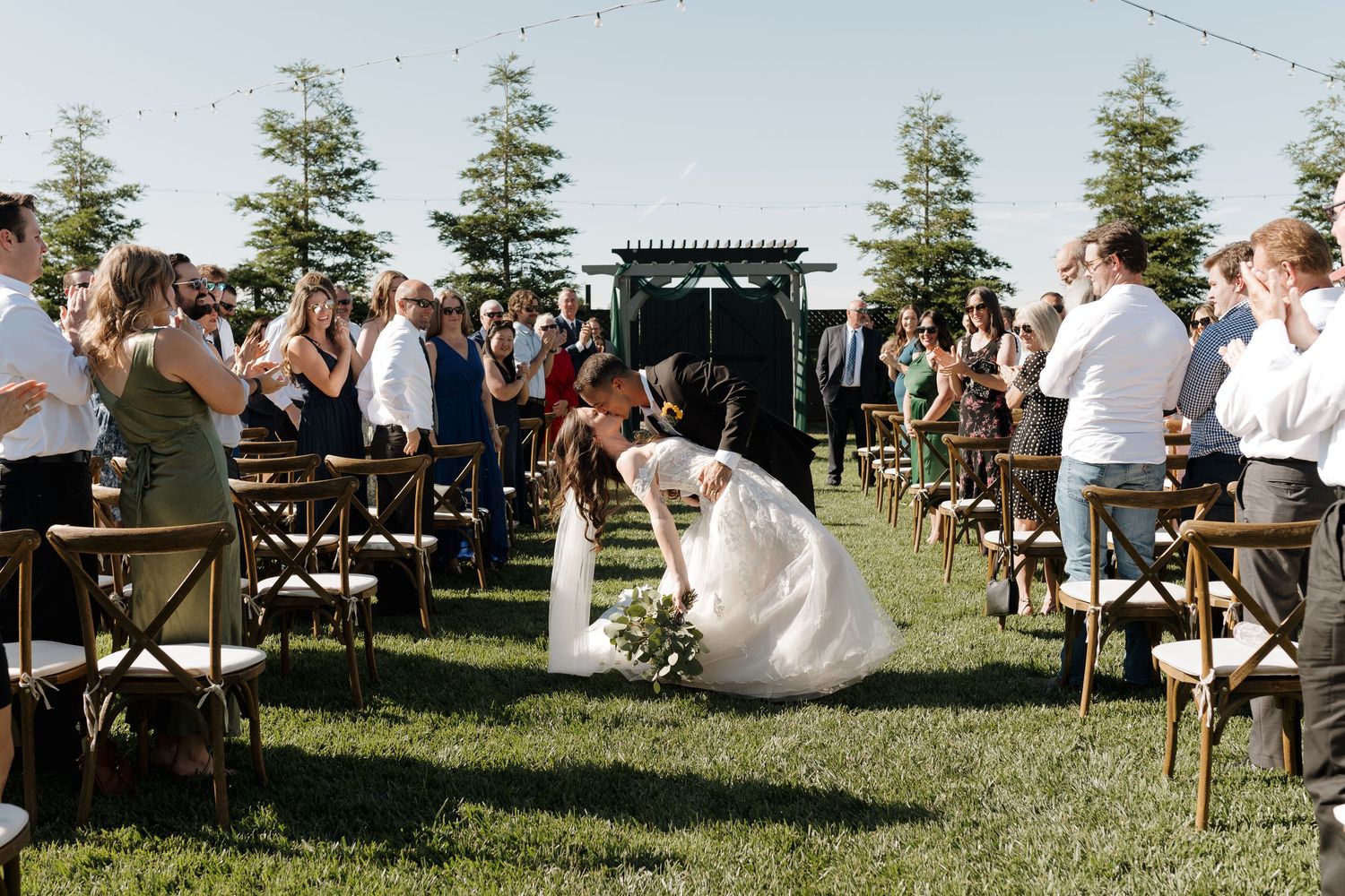 An outdoor wedding ceremony setup with white chairs arranged in rows against a backdrop of tall pine trees.