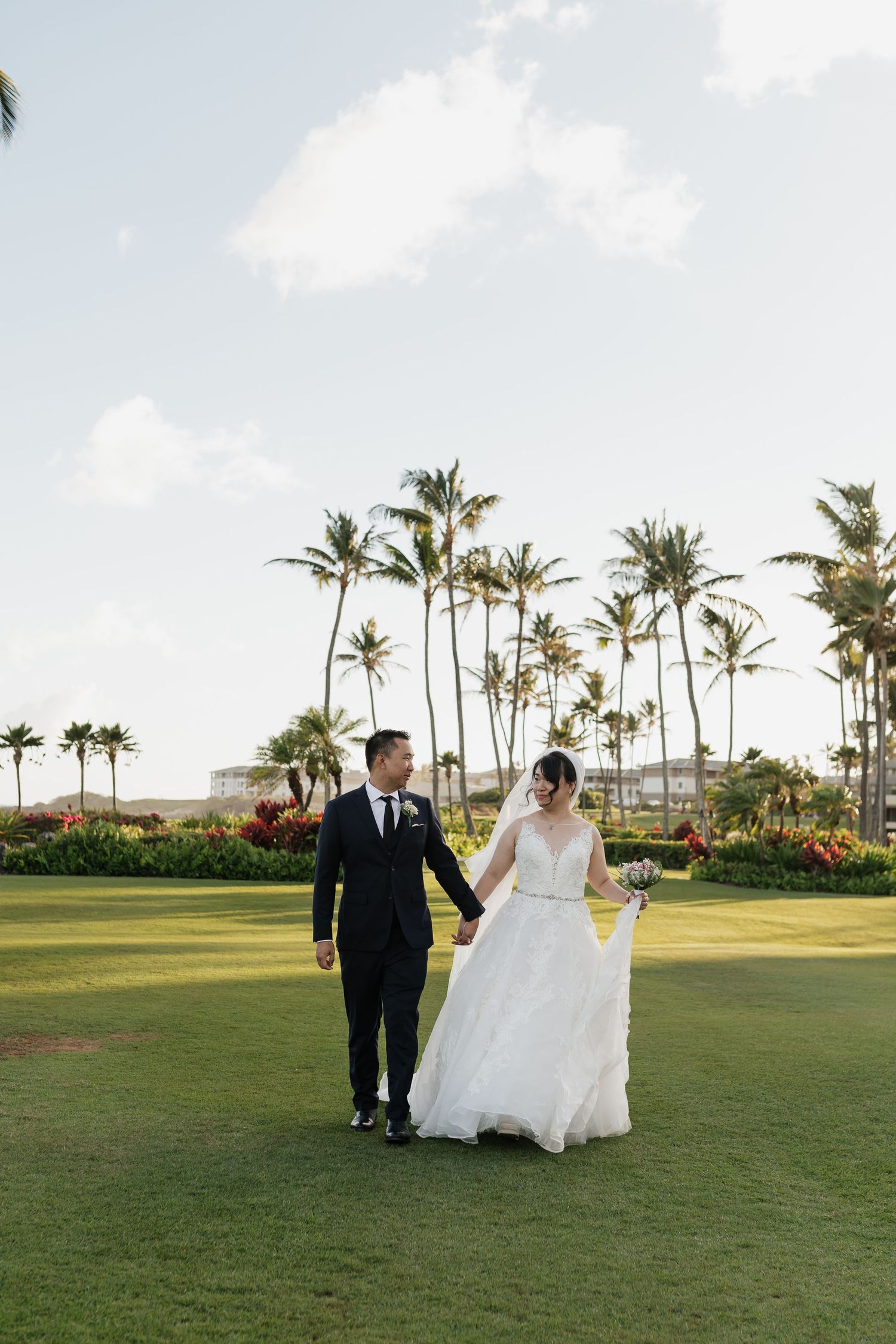 Couple strolling hand in hand on a lush green lawn with tropical palm trees in the background.