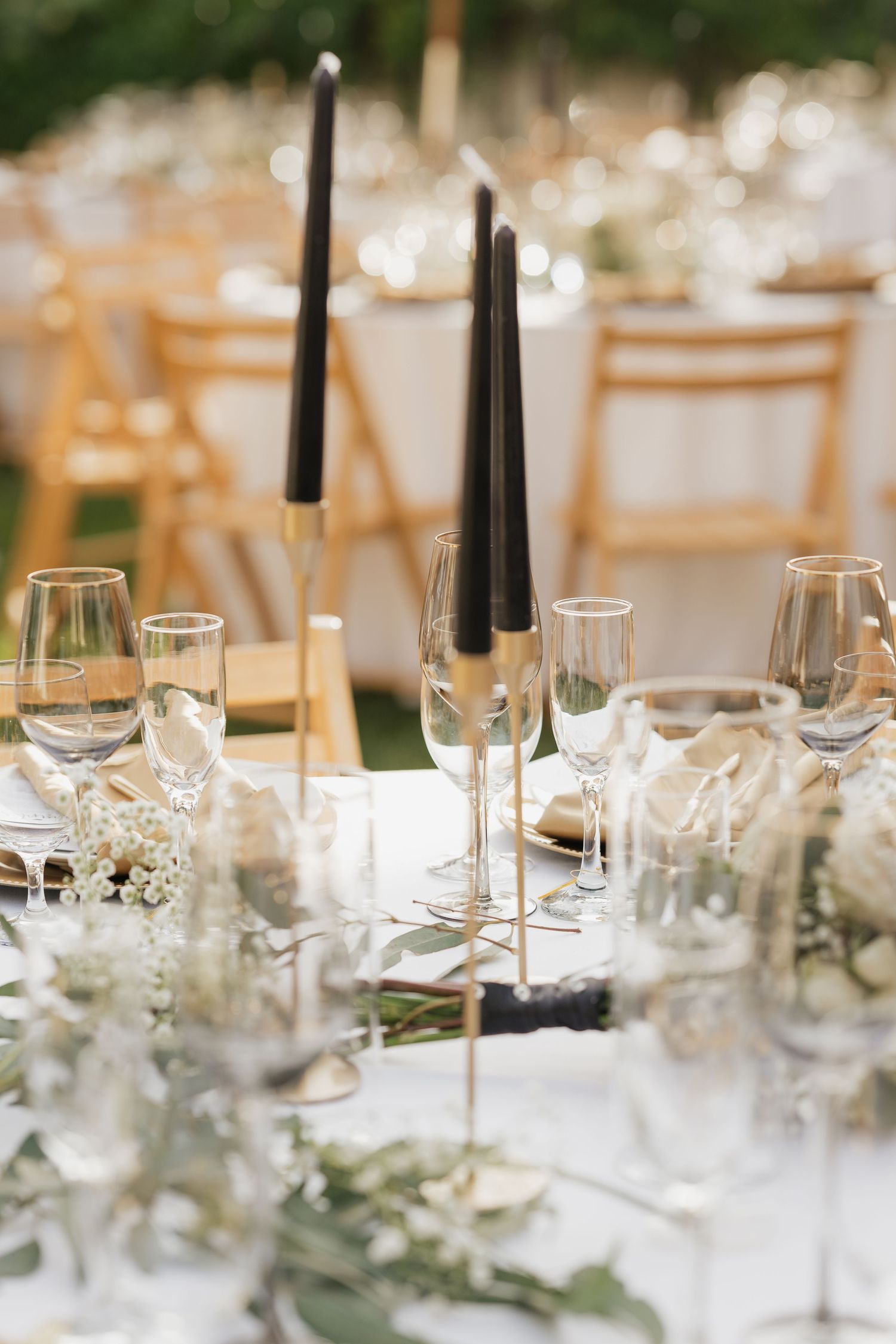 Elegant table settings with black taper candles, crystal glassware, and greenery centerpieces.
