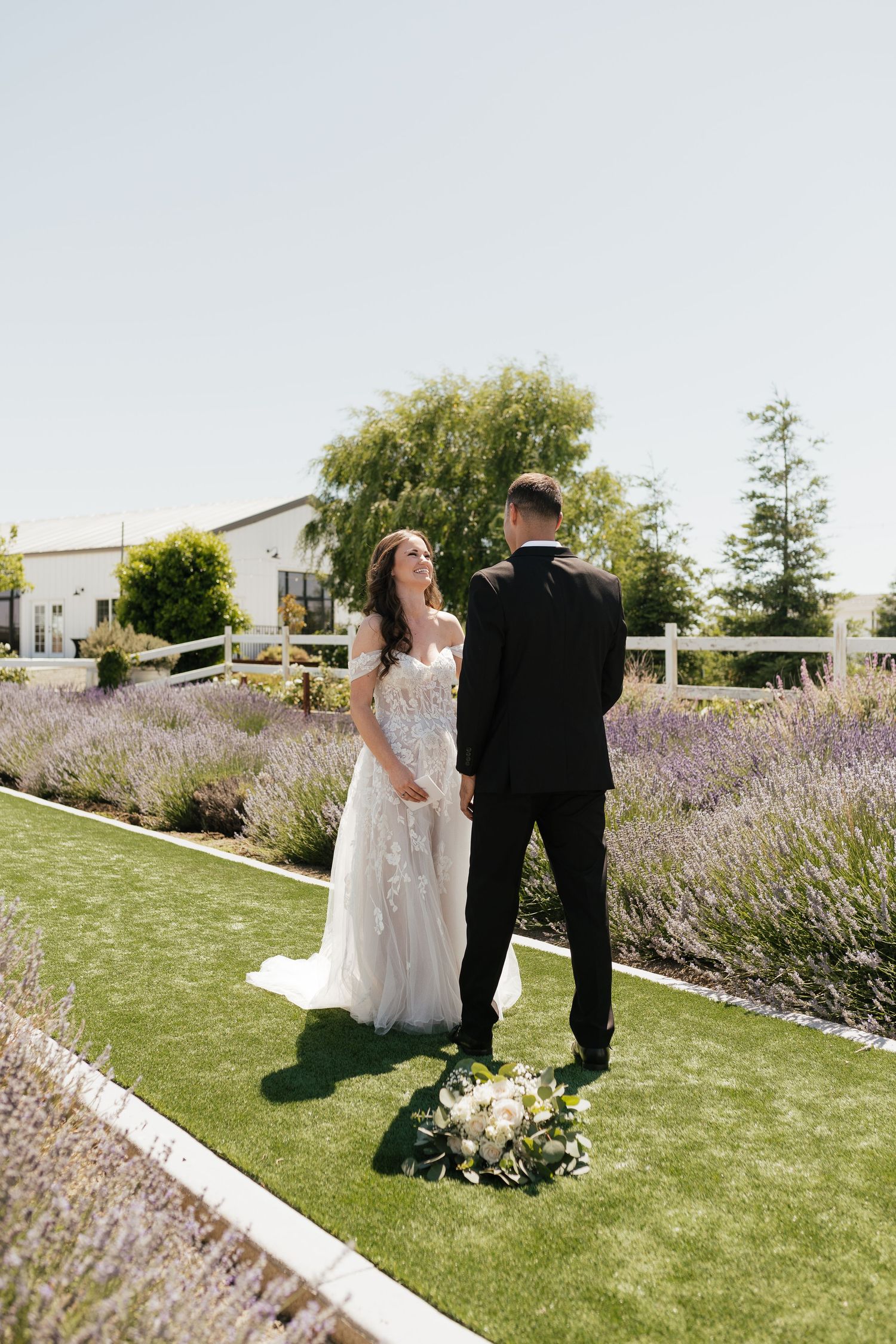 Wedding couple walking along a manicured lawn bordered by blooming lavender gardens.