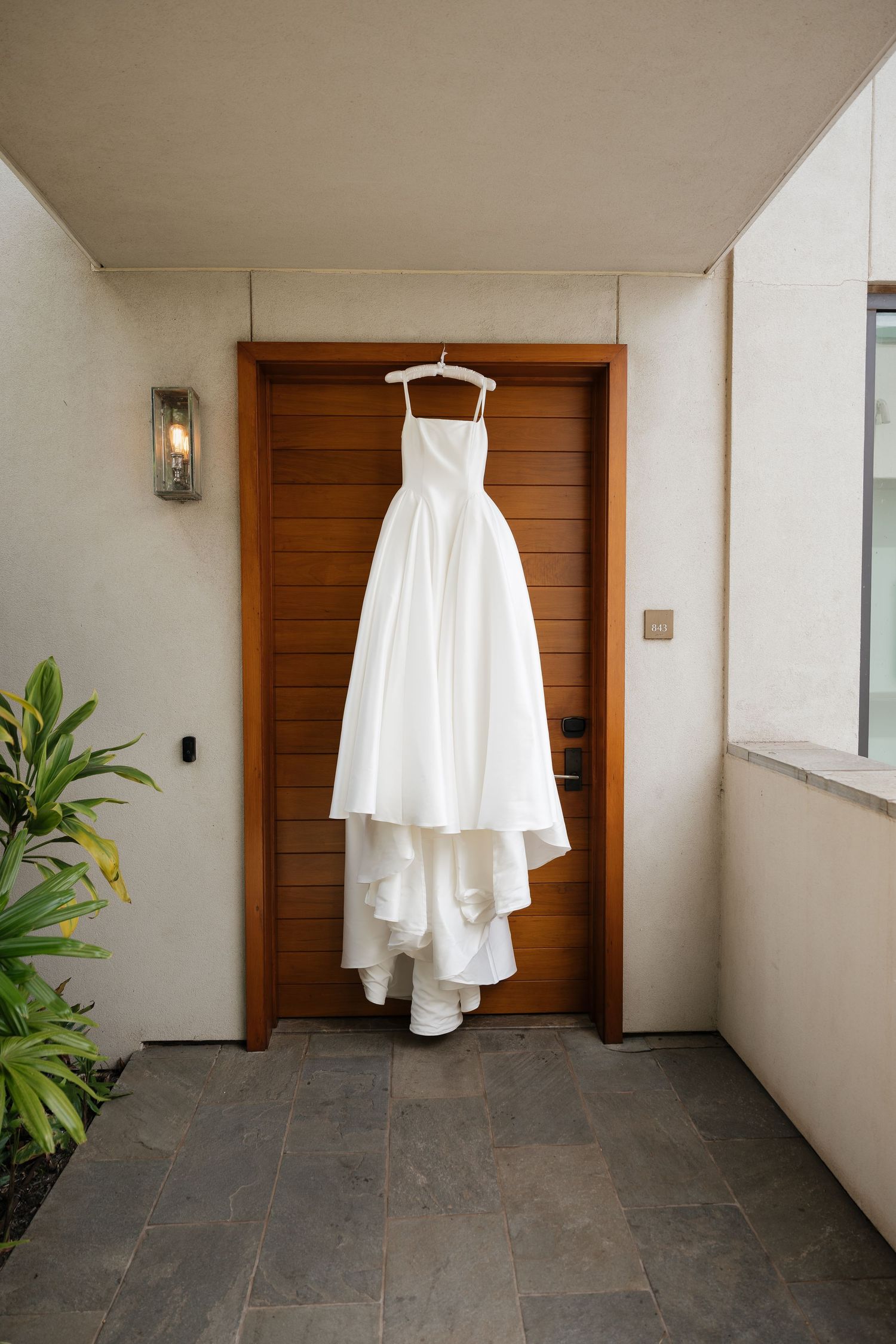 Wedding dress hanging in modern hallway with wooden doors and minimalist decor.