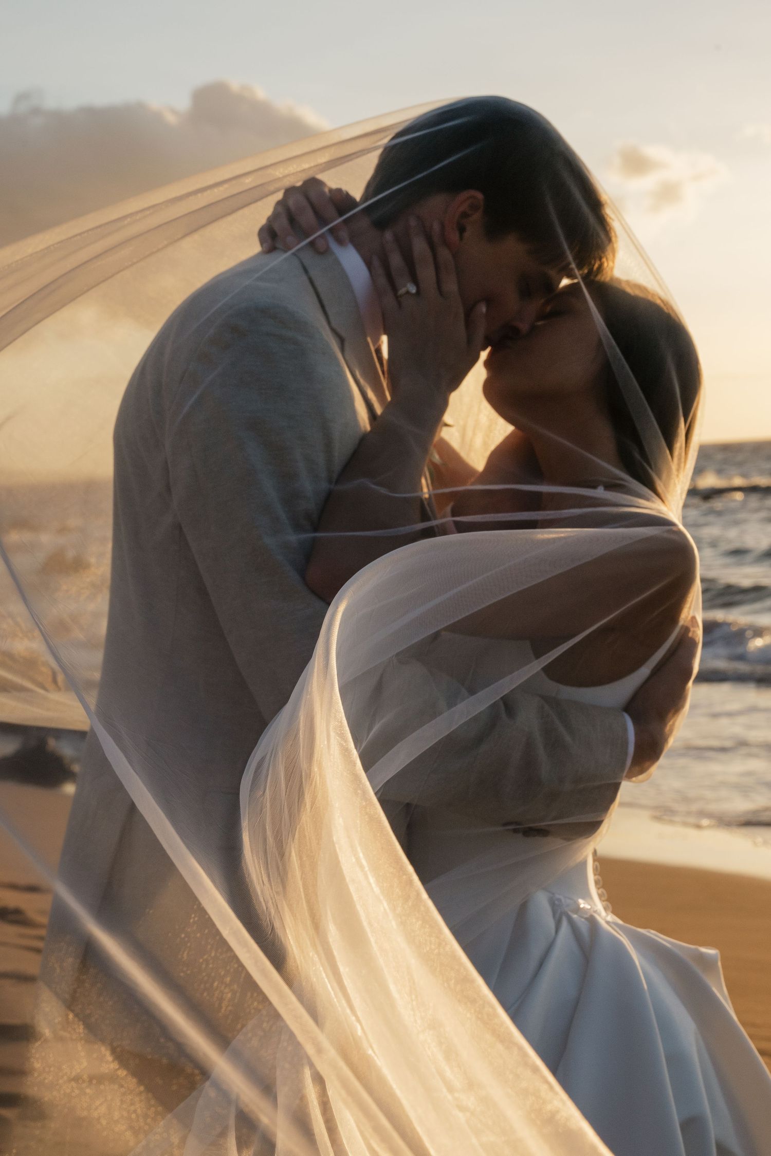Romantic sunset beach wedding photoshoot with flowing veil and warm golden light.