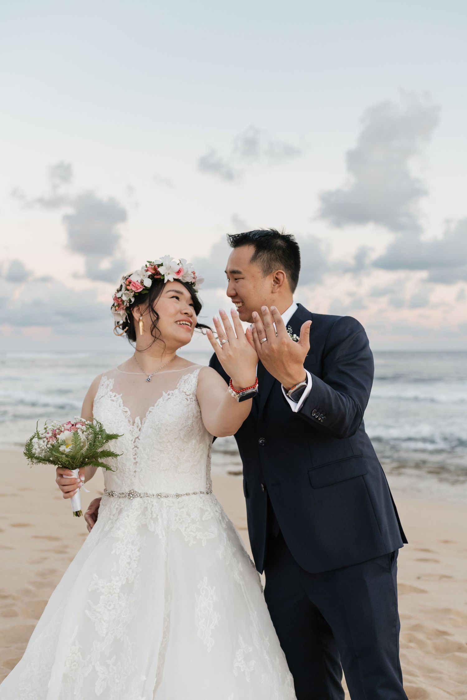 Wedding couple sharing joyful moment on beach with ocean waves in background.