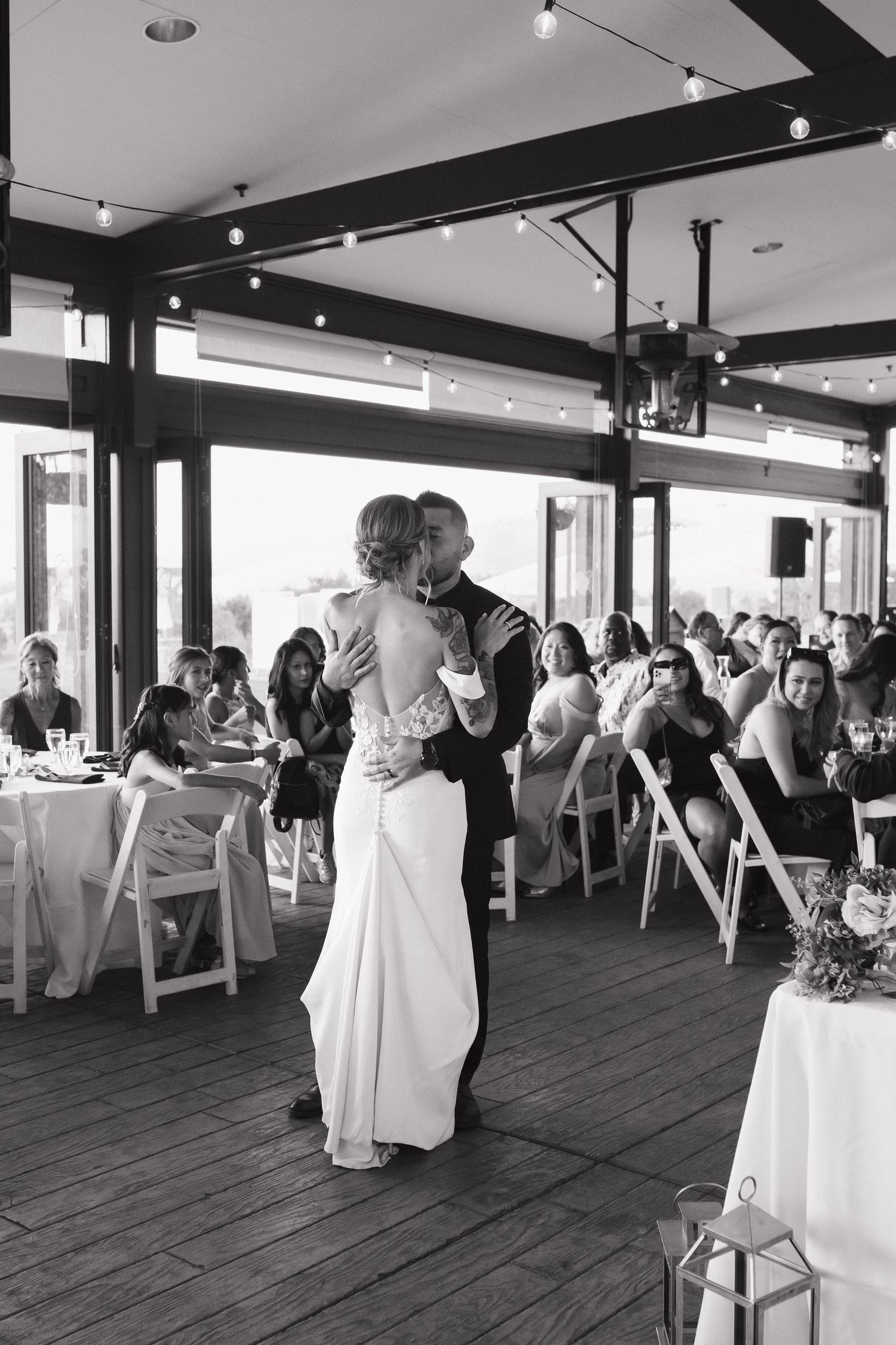 Black and white photo of wedding reception with couples dancing on wooden floor.
