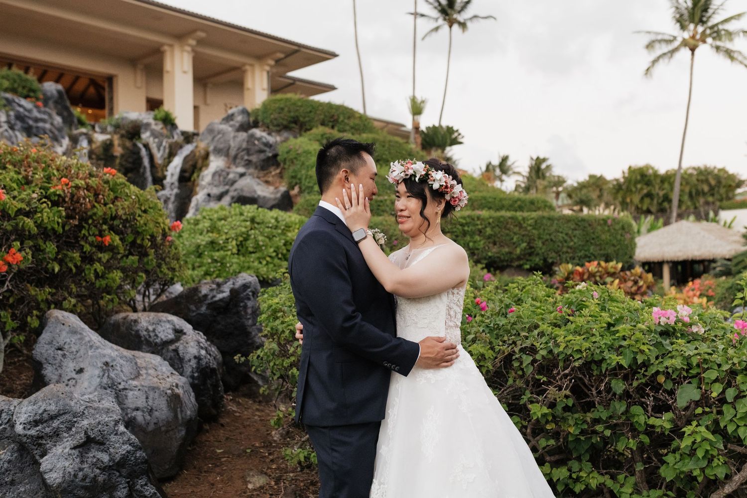 Wedding couple embracing near tropical gardens with lava rock landscaping.