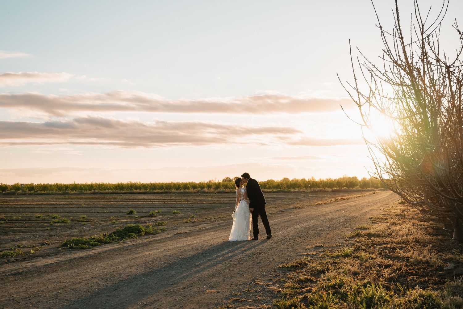 Silhouettes against sunset during outdoor wedding photoshoot in open field.