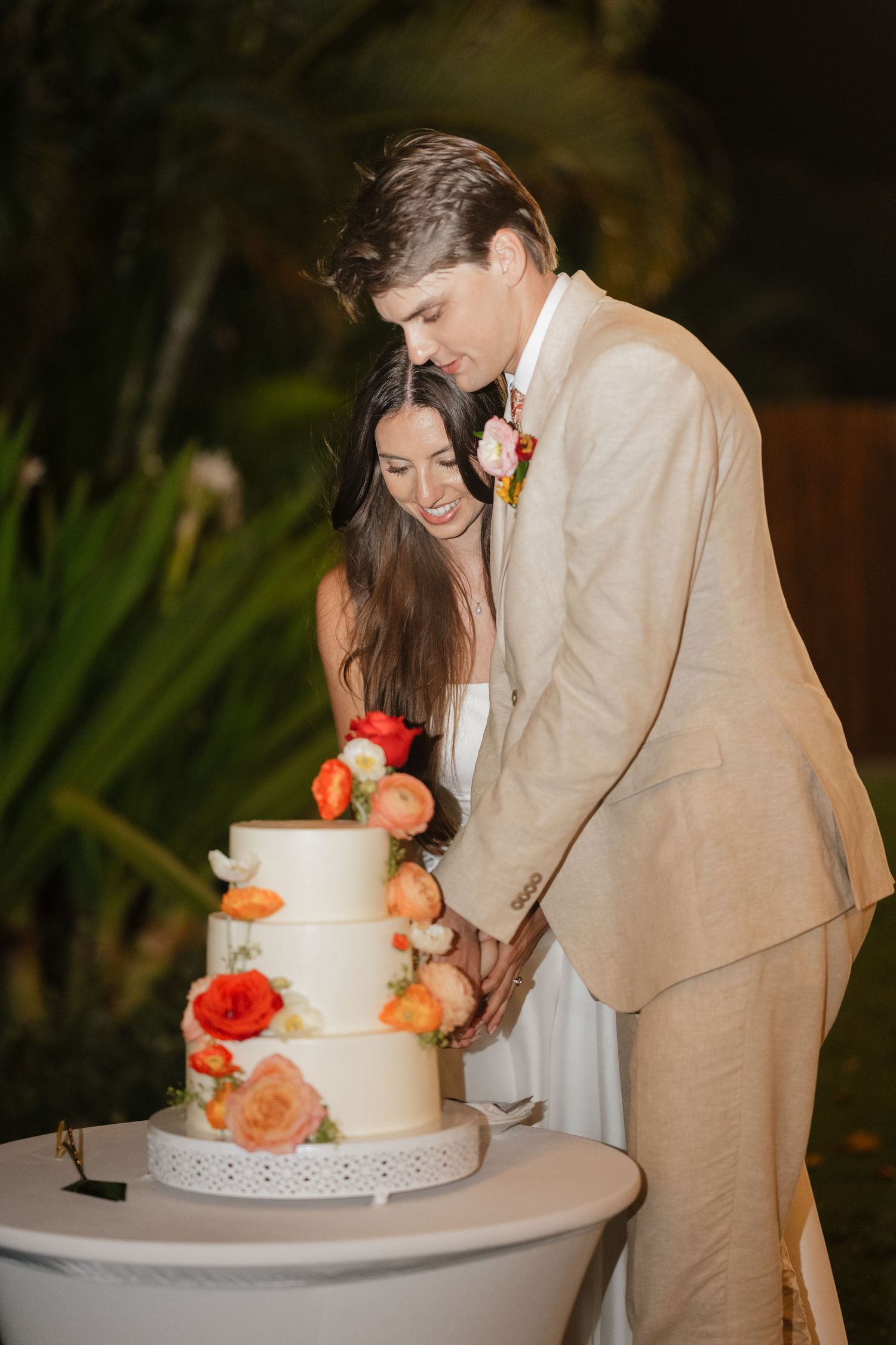 A couple cuts their elegant white wedding cake adorned with coral and peach flowers at their reception.