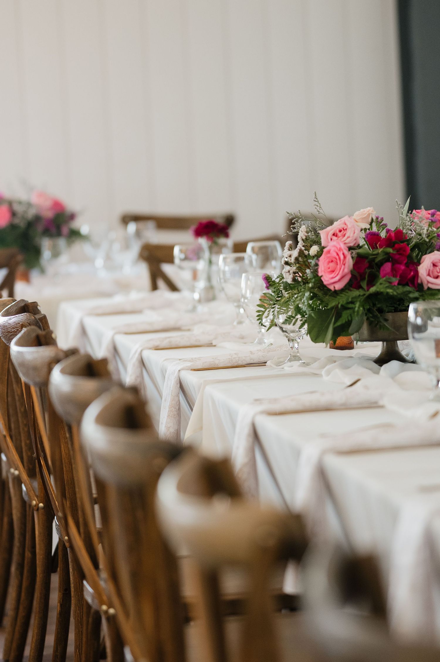An elegant wedding reception table setting with pink roses and wooden chairs.