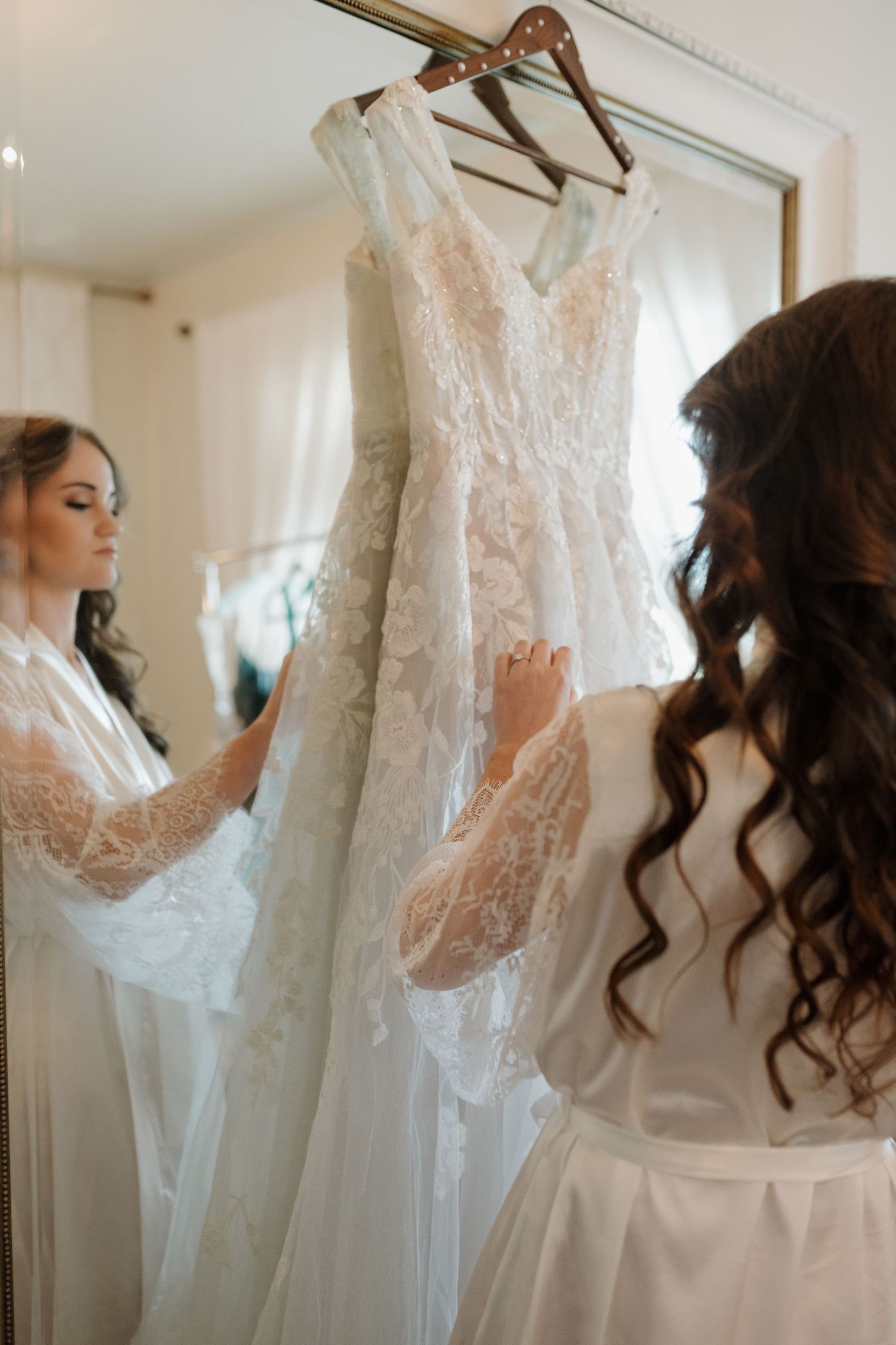 Wedding dress details showing lace bodice and veil hanging in preparation room.
