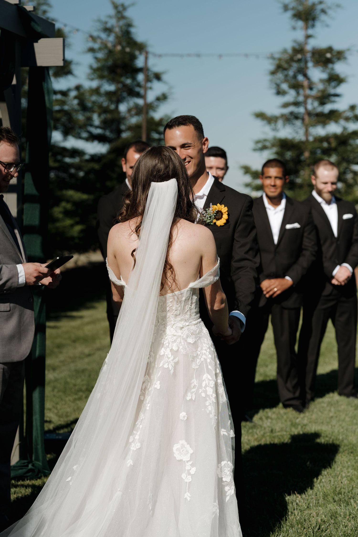 Wedding party gathers on a grassy hill with bridesmaids in flowing dresses and groomsmen in dark suits.