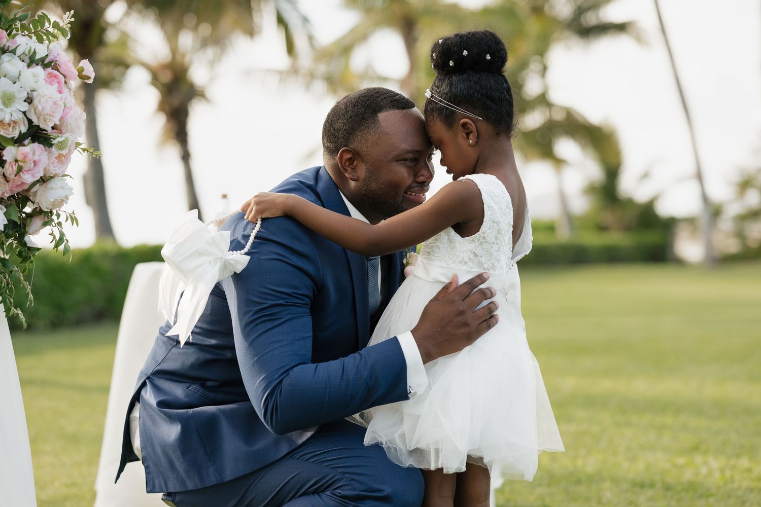 Intimate wedding ceremony moment under a white canopy with tropical palm trees in the background.