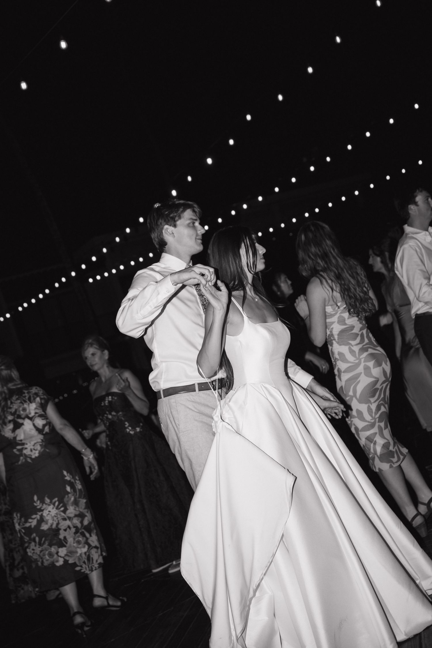 Wedding reception dance floor with string lights overhead and guests dancing in black and white.