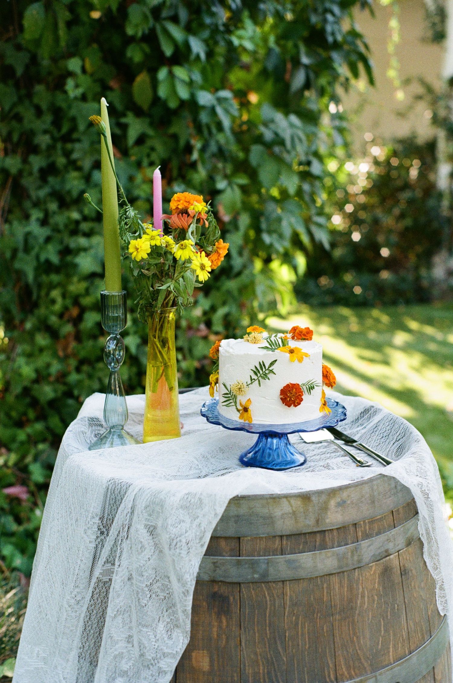 A rustic wine barrel decorated with white lace tablecloth and fresh flowers creates an elegant outdoor party setting.