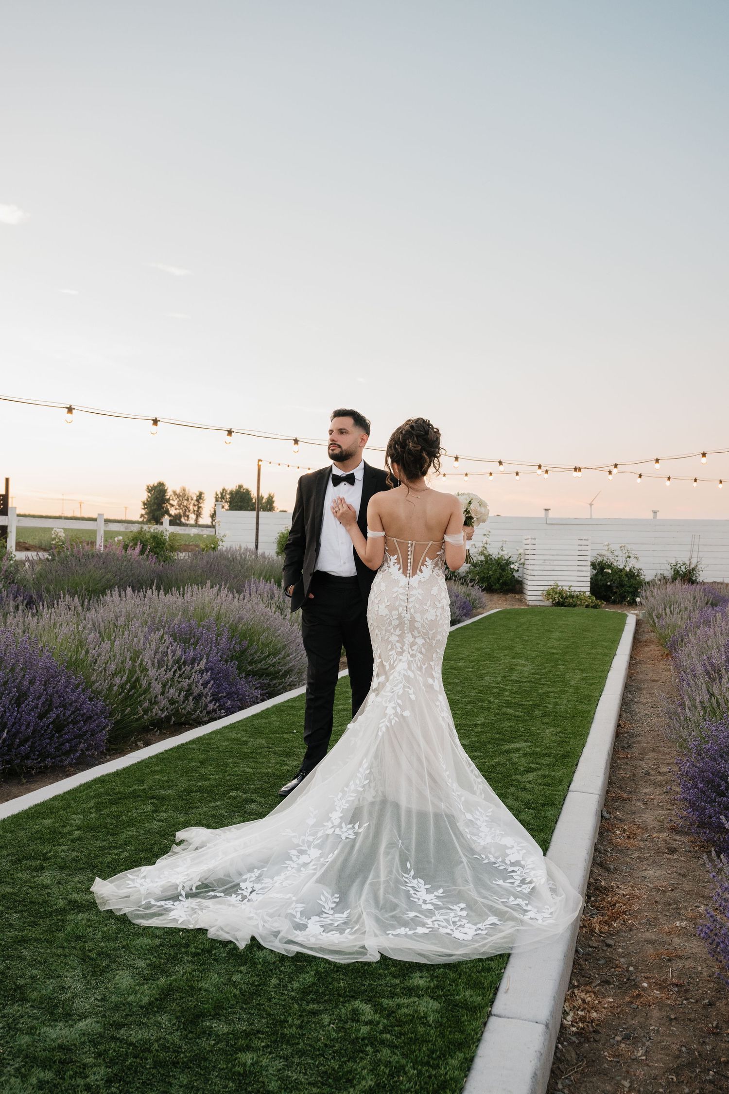 Couple walking through garden path lined with blooming lavender at sunset.