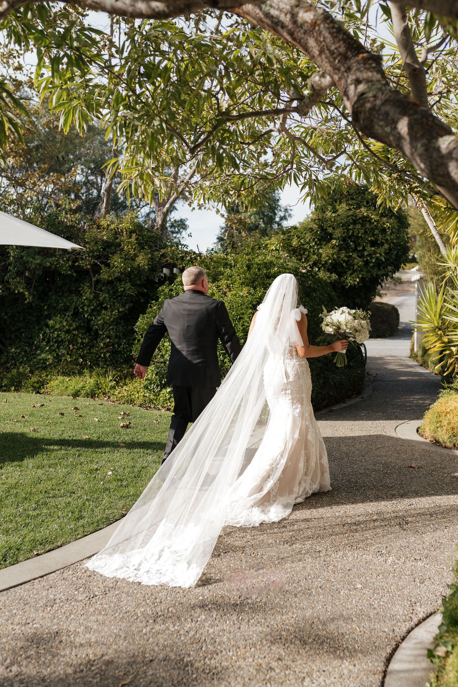 A dramatic cathedral veil trails behind on a winding garden walkway.