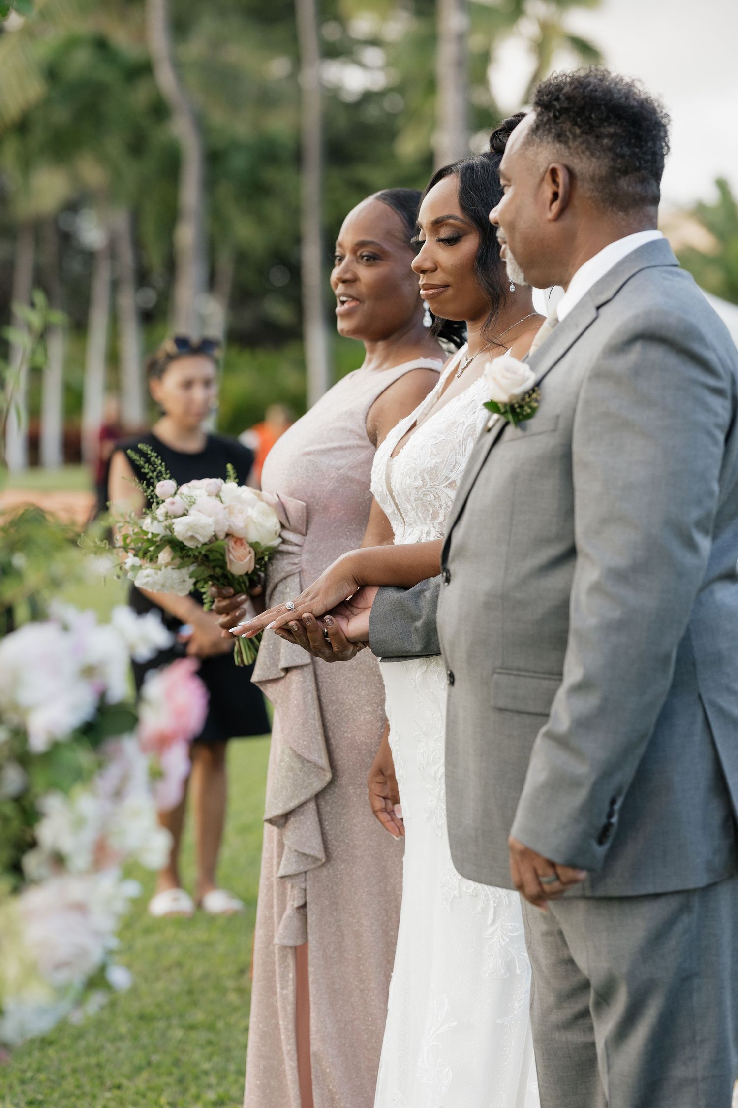 Wedding party in grey and pink attire standing together on grassy lawn.