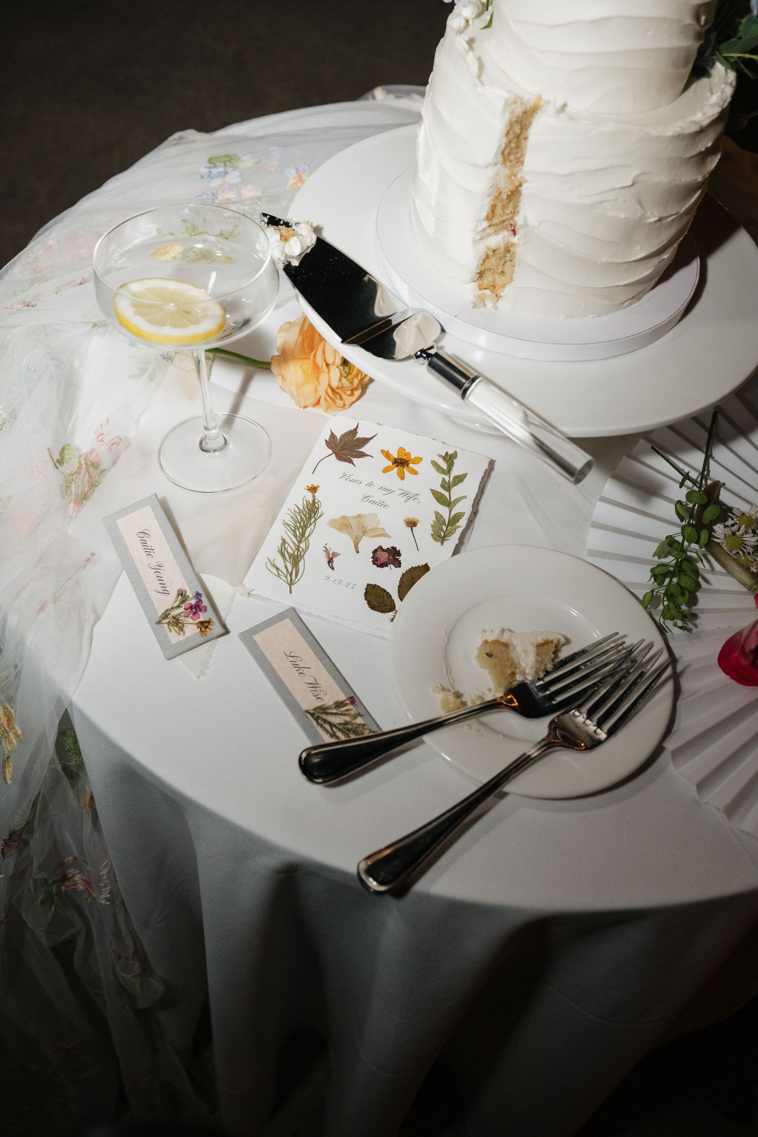 Wedding reception table settings with white linens, scattered floral decorations, and place cards on an elegant round table.