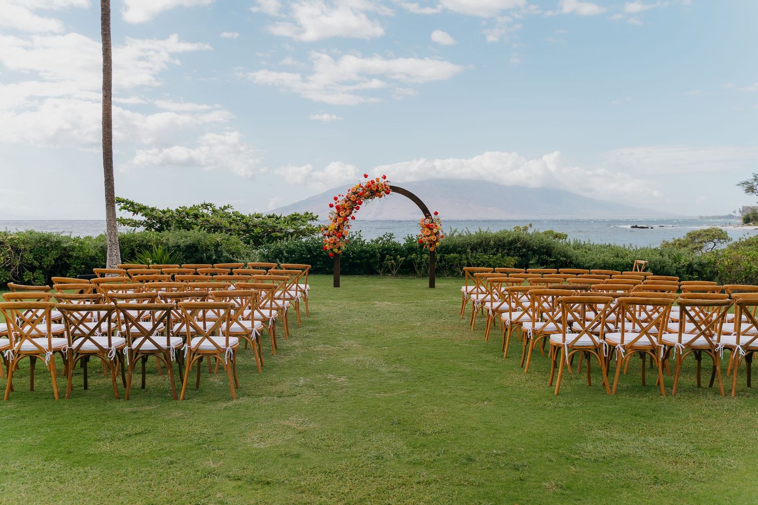 Rows of wooden cross-back chairs set up on a lush green lawn for an outdoor wedding ceremony with mountain views.
