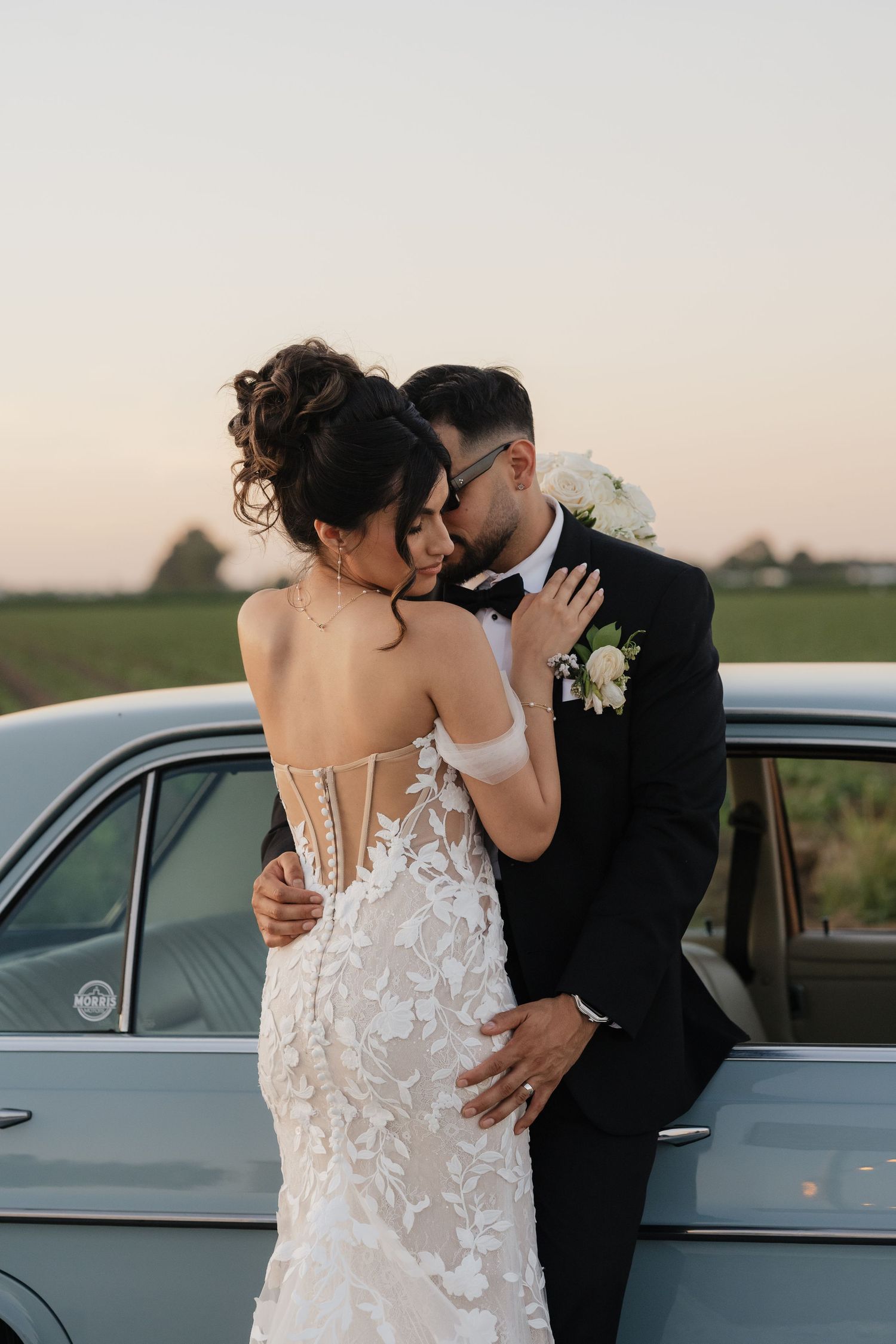 A romantic wedding photo session featuring a couple embracing by a vintage car at sunset.
