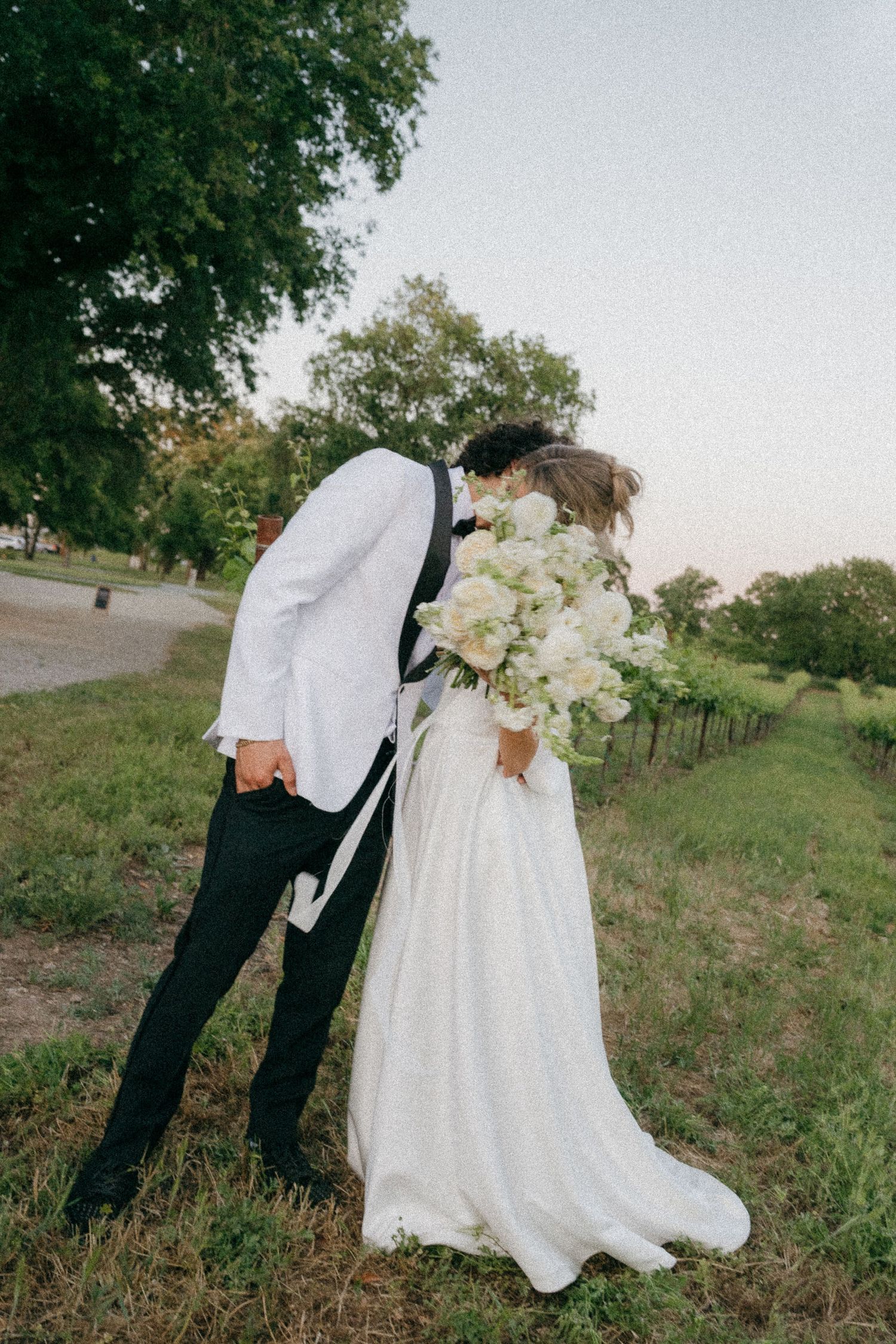 A wedding couple poses playfully in a grassy outdoor setting showing off their formal attire.