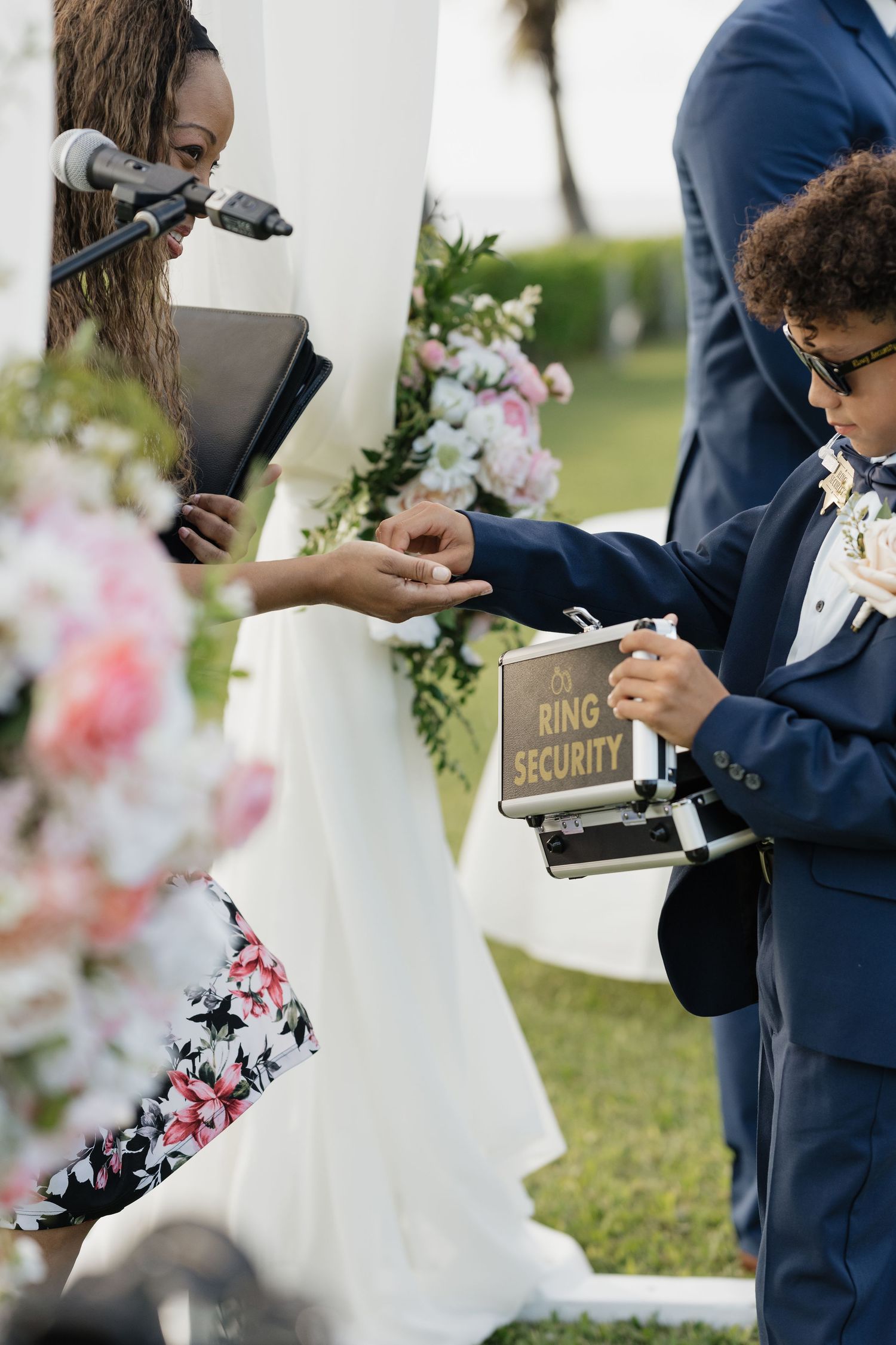 Wedding ceremony details showing ring security box and floral decorations at outdoor venue.